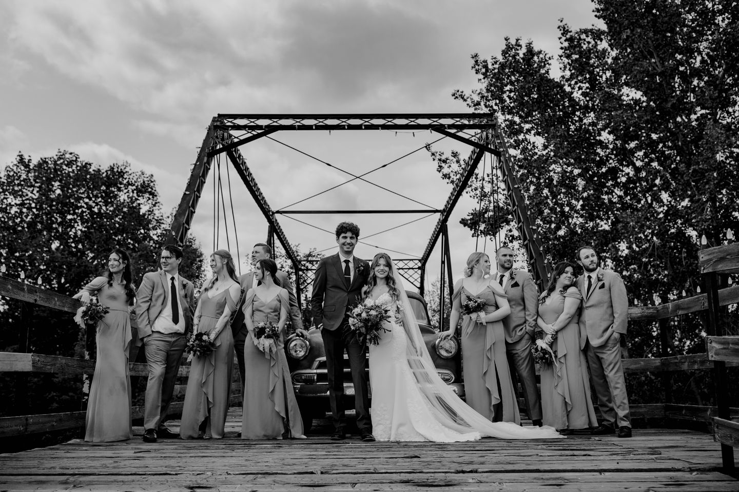 Wedding party poses on rustic bridge in black and white photography.