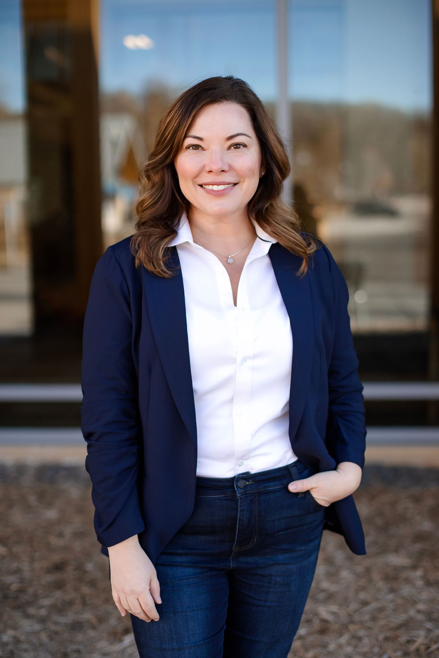 Professional headshot of person in navy blazer and white shirt standing outdoors.
