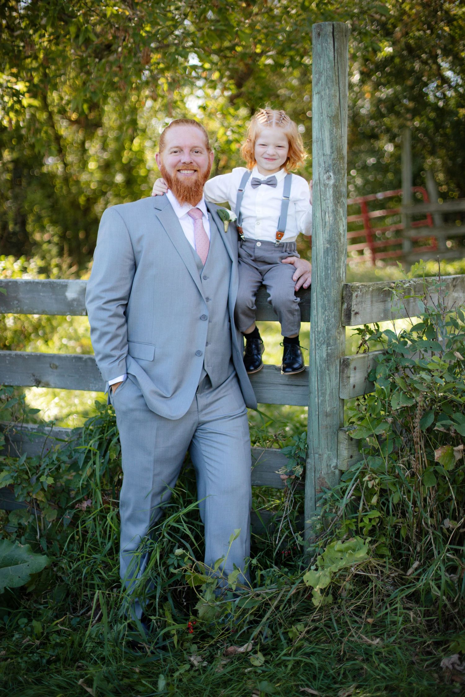 A formal outdoor portrait by a rustic wooden fence surrounded by lush greenery on a sunny day.