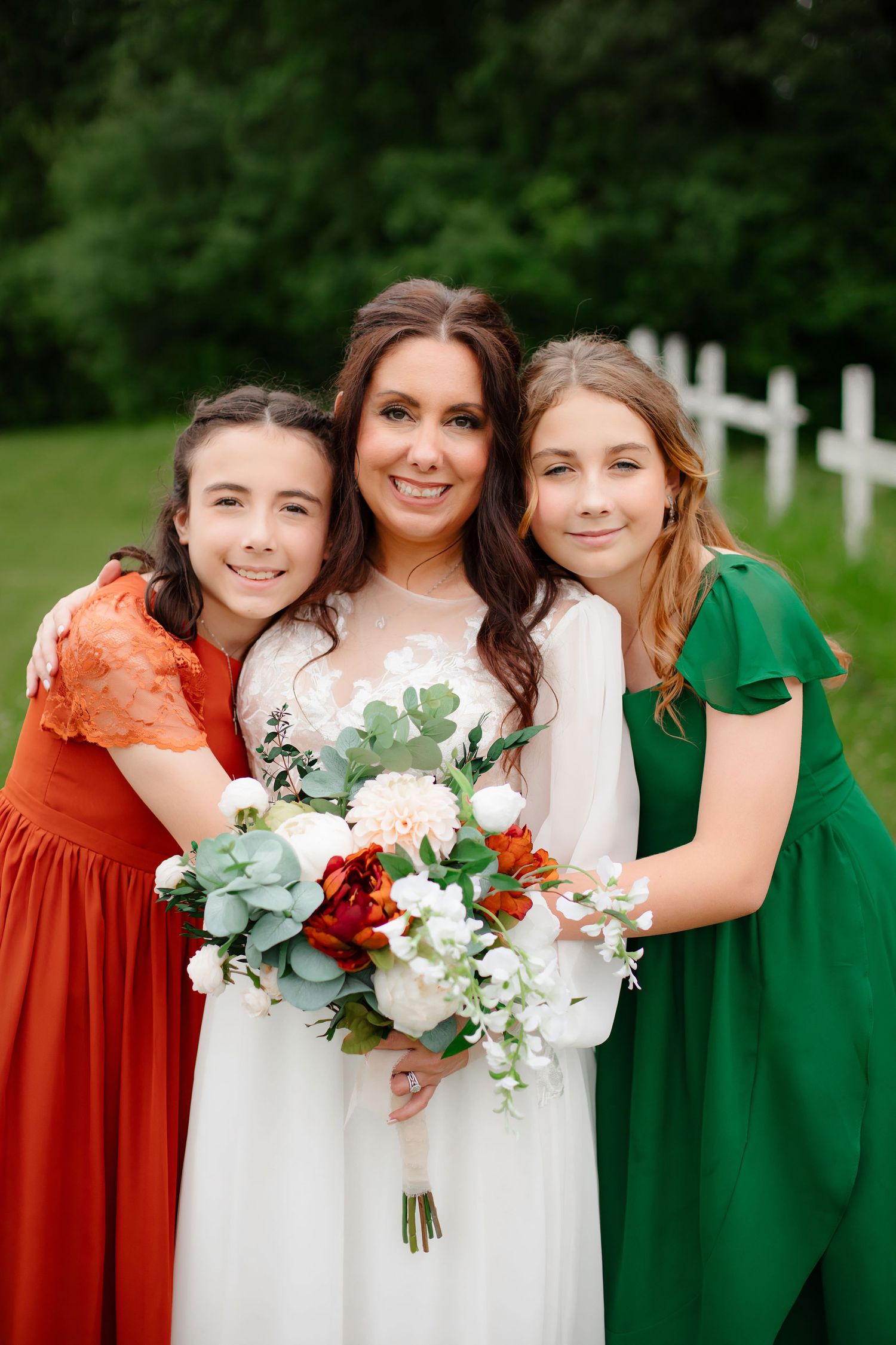 Bridal party in alternating green and orange dresses poses with bouquets outdoors.