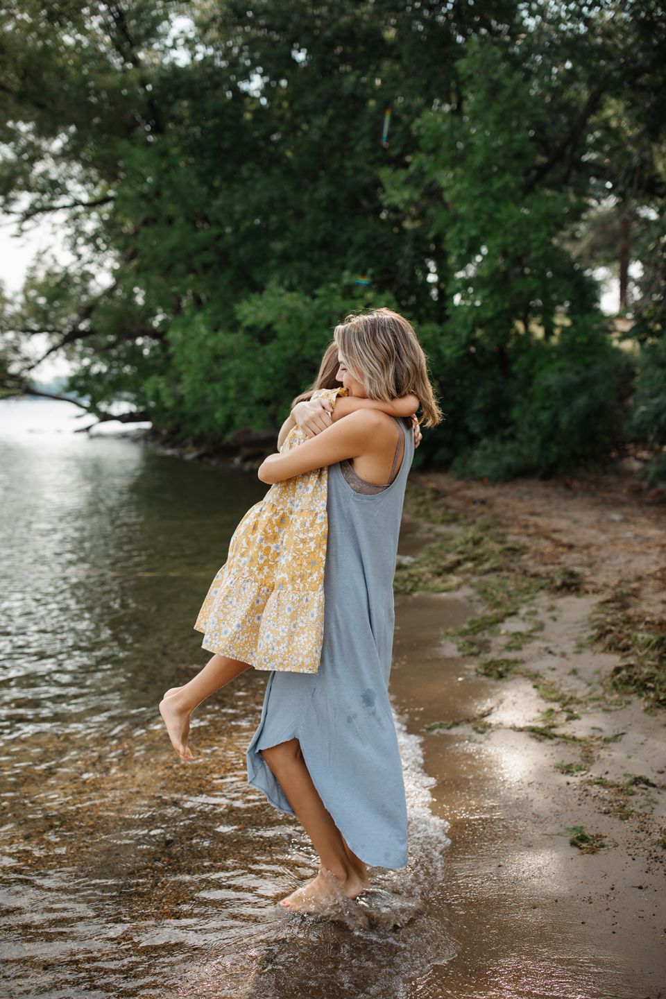 A tender embrace captured between parent and child playing in the shallow waters of a lake on a summer day.