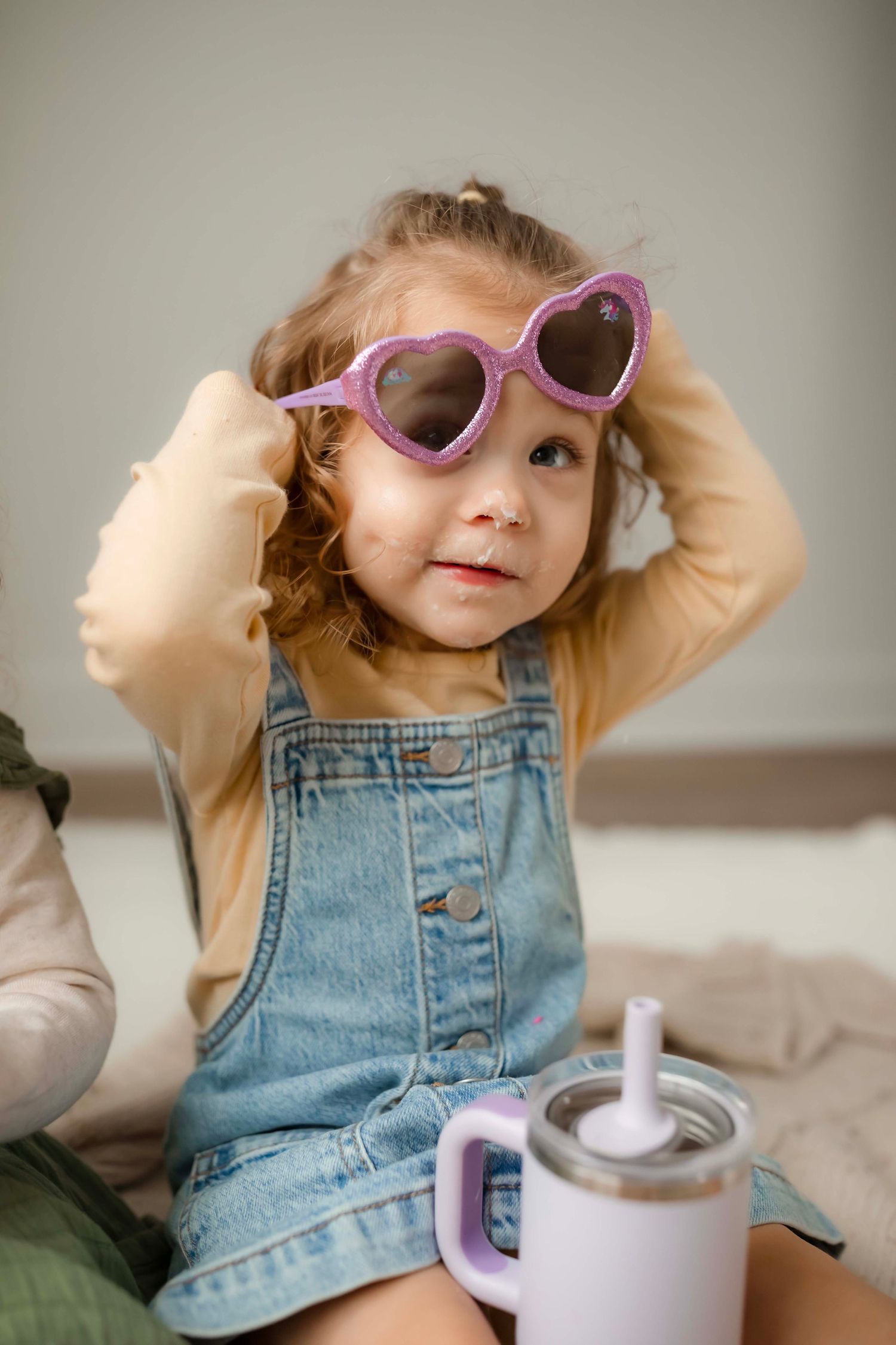 Child in overalls and heart sunglasses plays with a teapot during playtime.