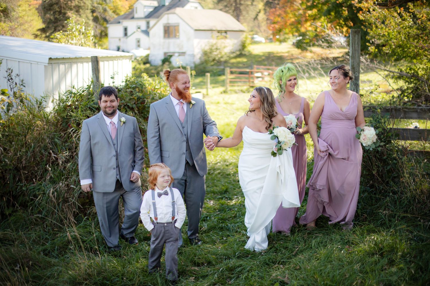 Wedding party in gray suits and purple dresses poses together outdoors in autumn setting.