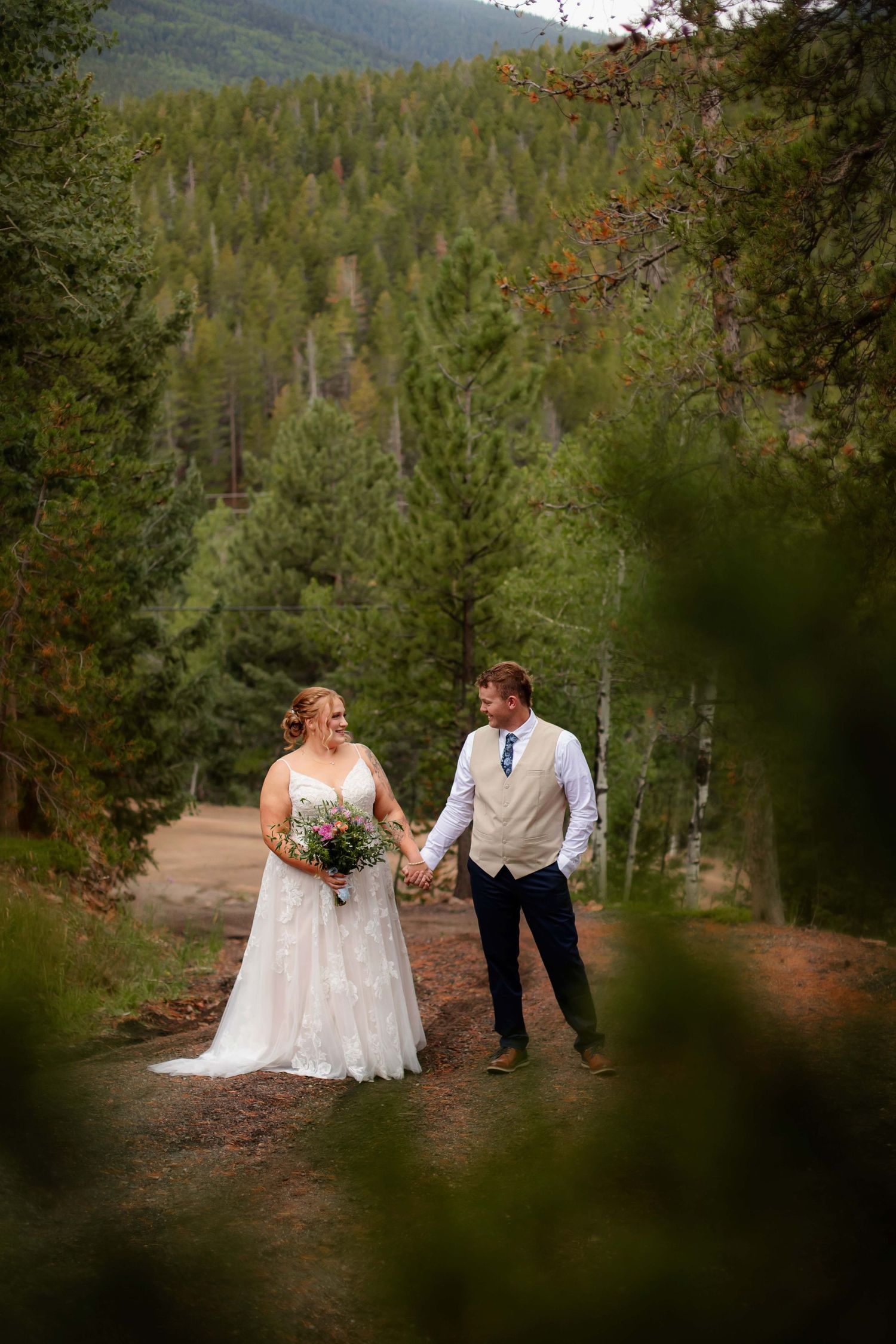 A couple shares a romantic moment in a mountain forest setting during their wedding celebration.