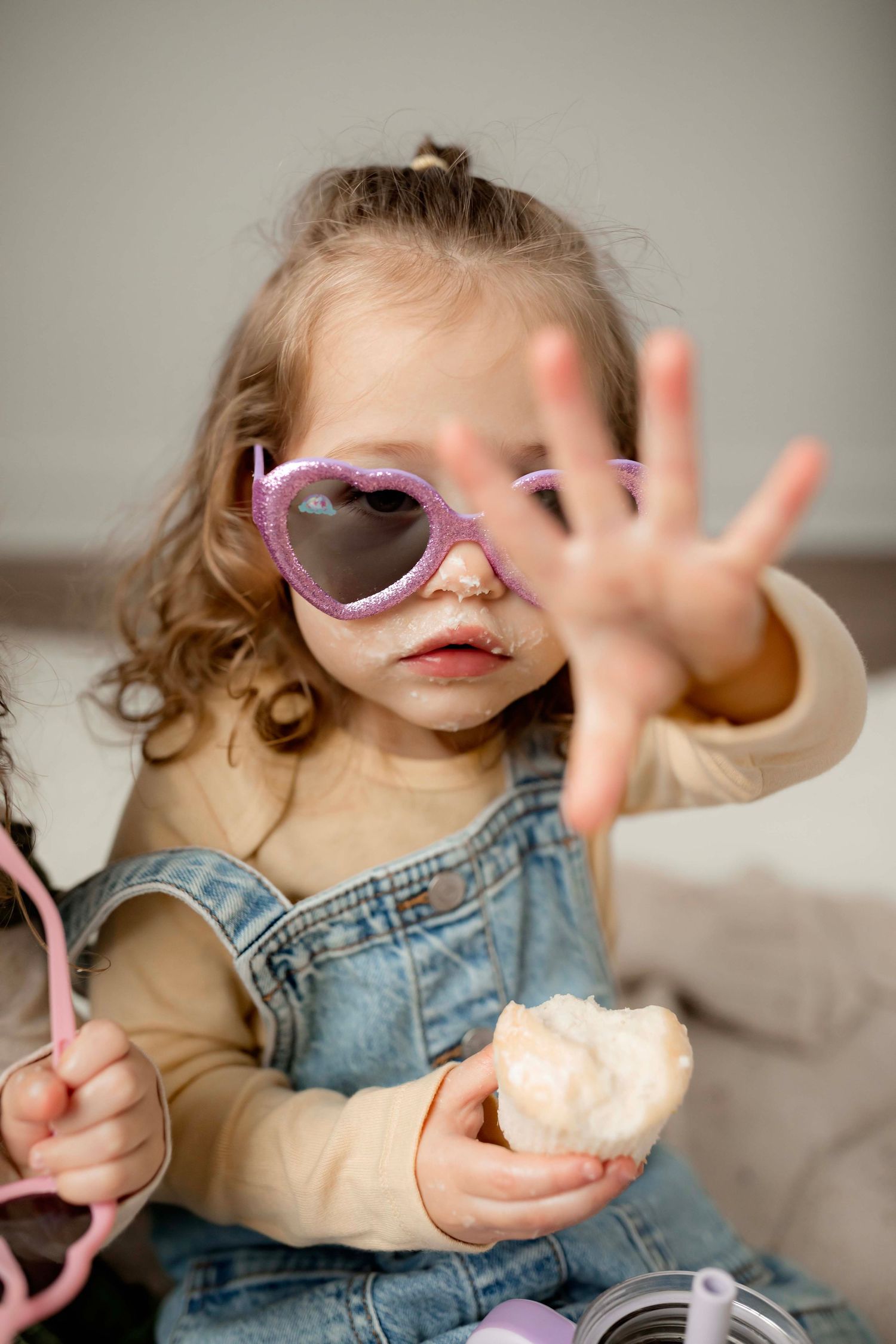 Small child in overalls and pink sunglasses makes expressive gestures while playing.