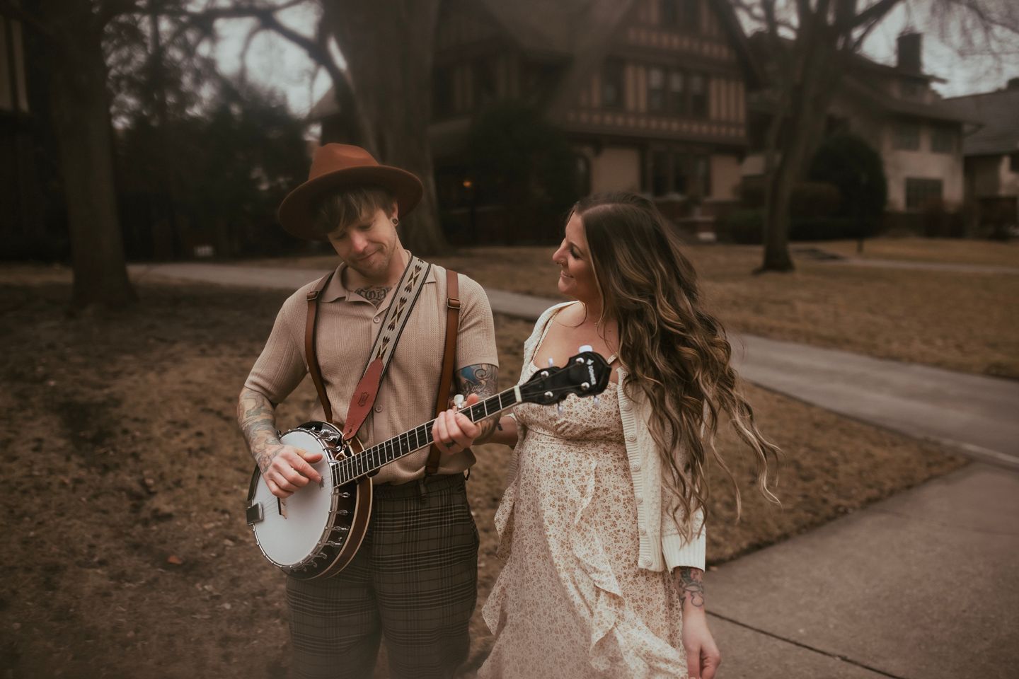 A couple in wedding attire dances together on a rustic path while someone plays banjo in the background.