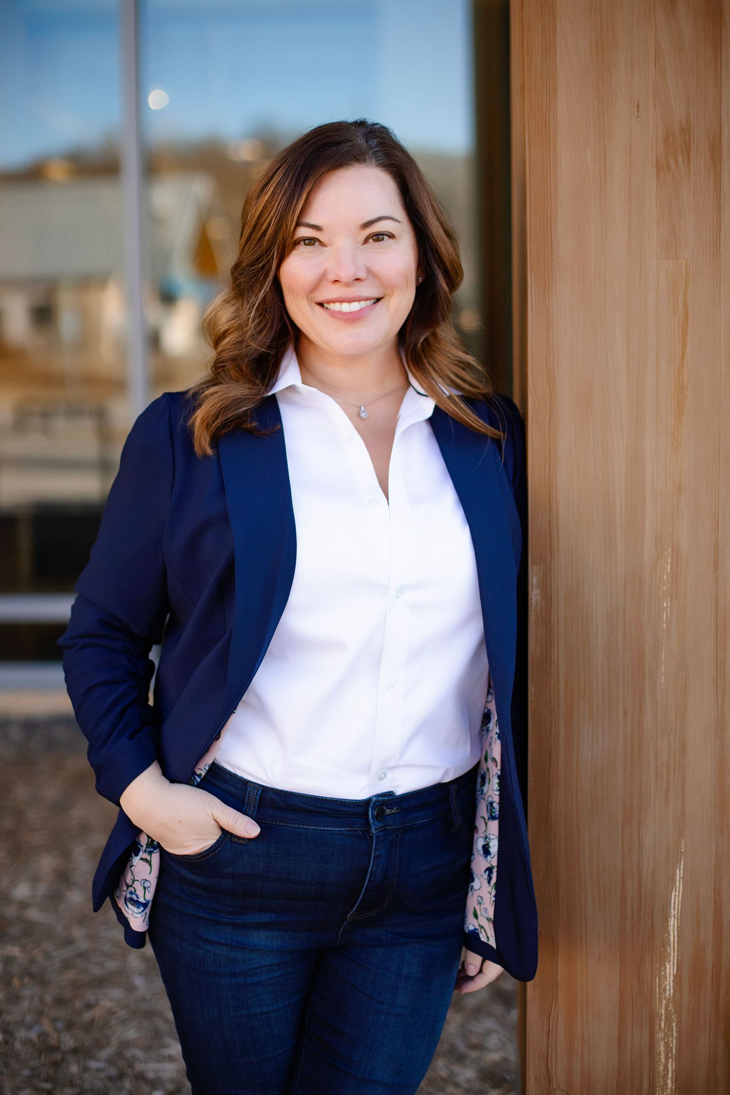 Business professional in navy suit and white shirt smiles warmly against modern building exterior.
