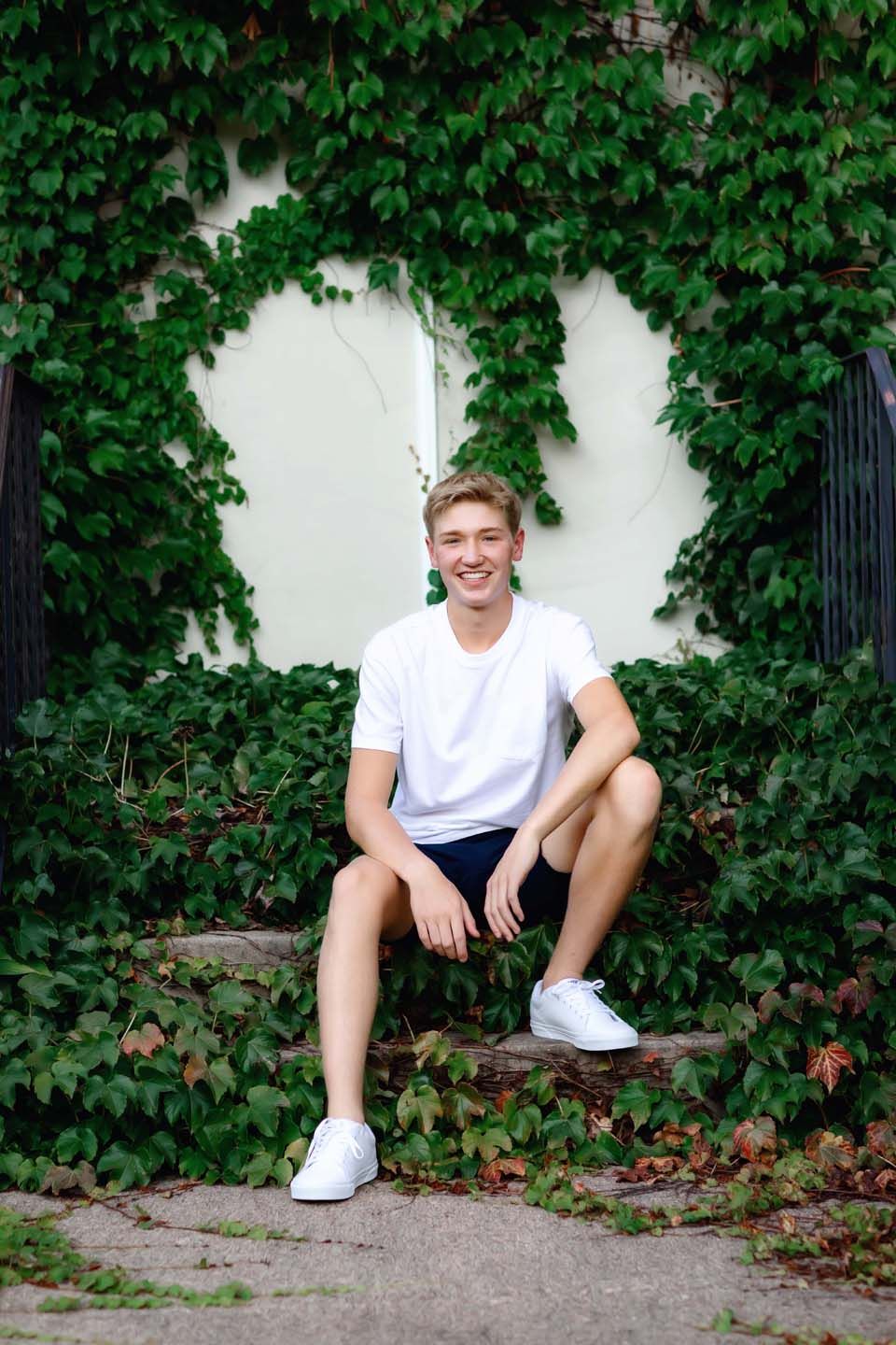 Summer portrait against ivy-covered wall wearing white t-shirt and navy shorts.