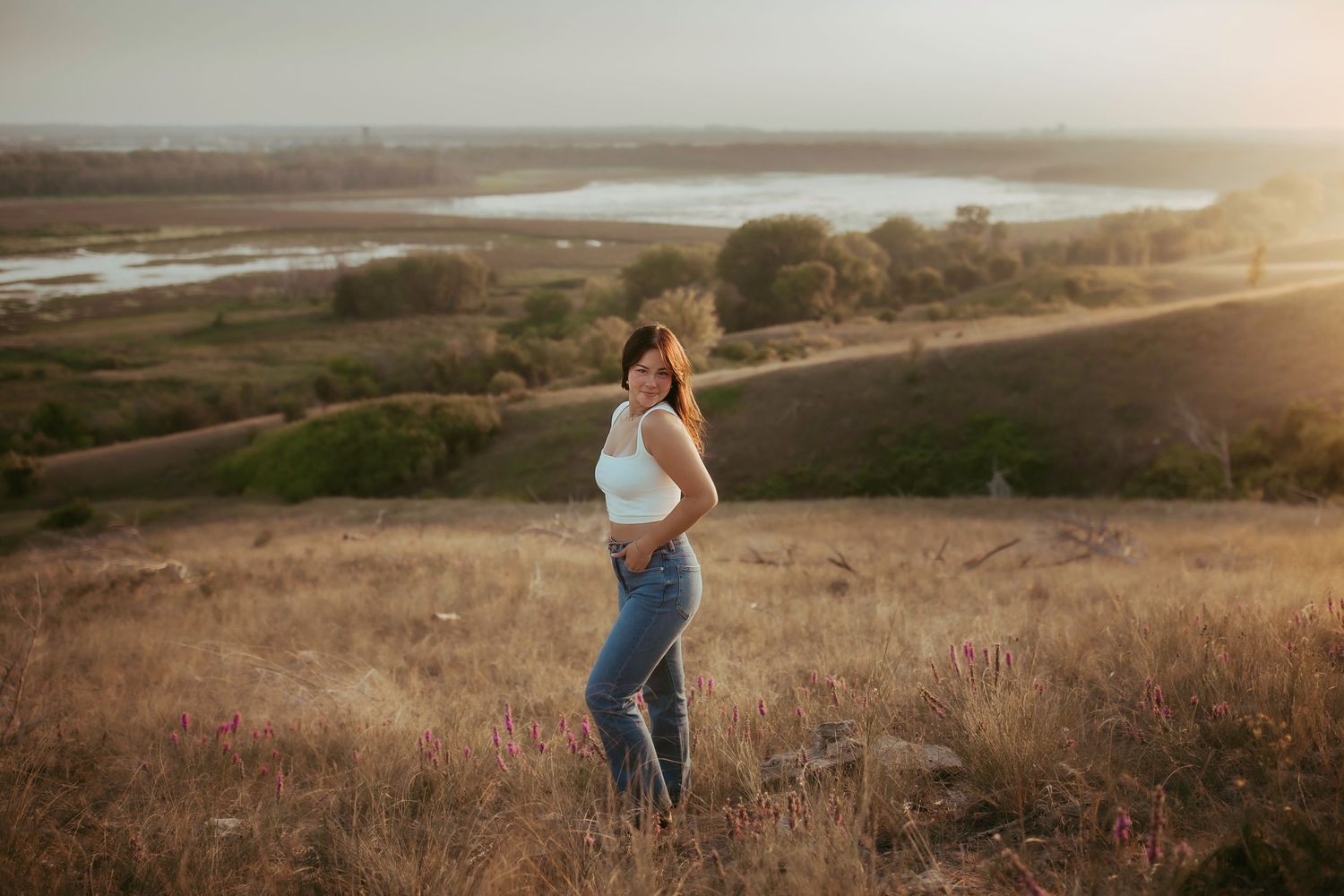 Woman in casual outfit poses against scenic valley view during golden hour.