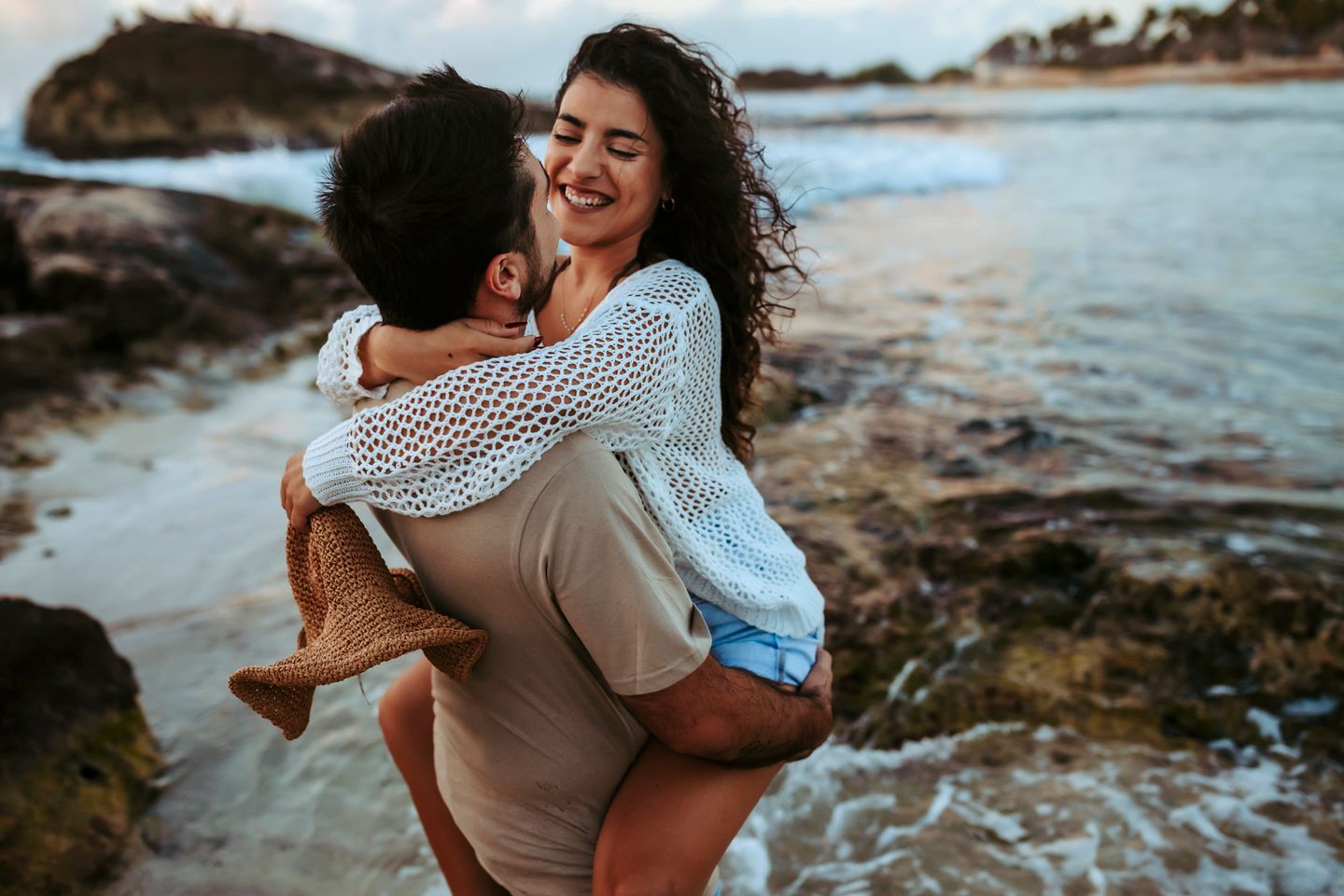 A loving piggyback ride moment captured against a scenic ocean backdrop at dusk.