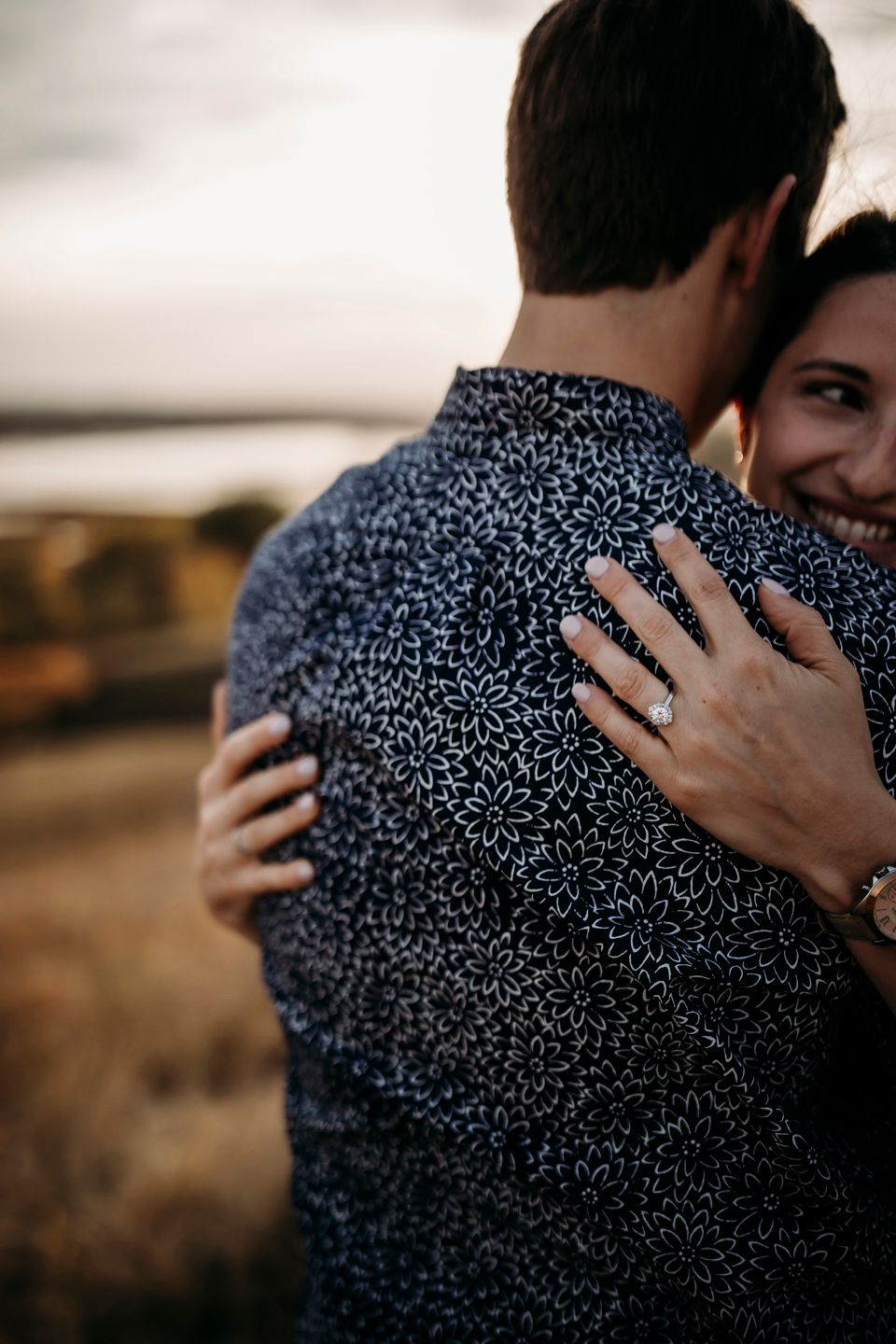 Intimate close-up showing hands with an engagement ring during an embrace.