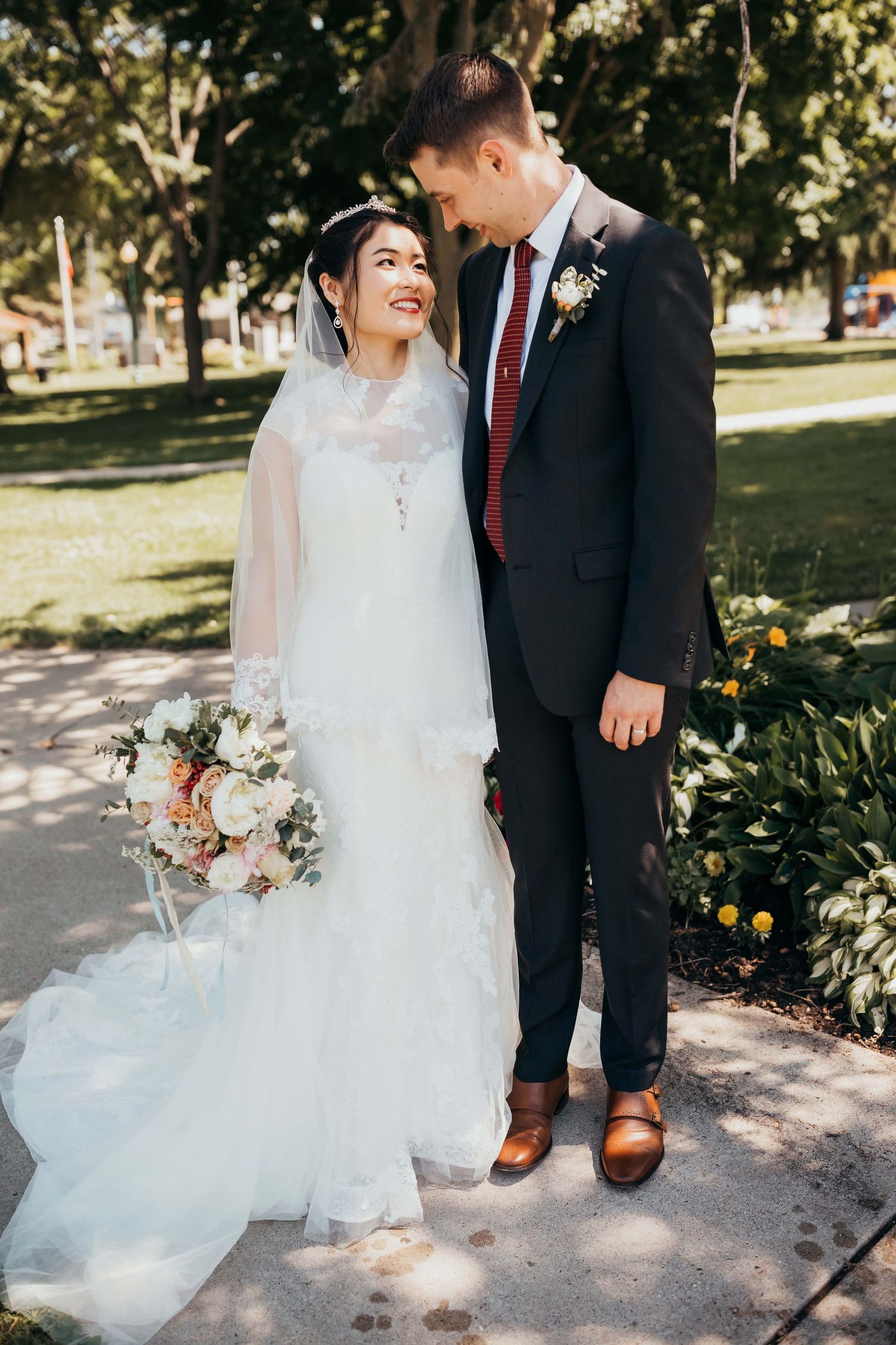 A romantic outdoor wedding portrait of a couple on a tree-lined garden path.