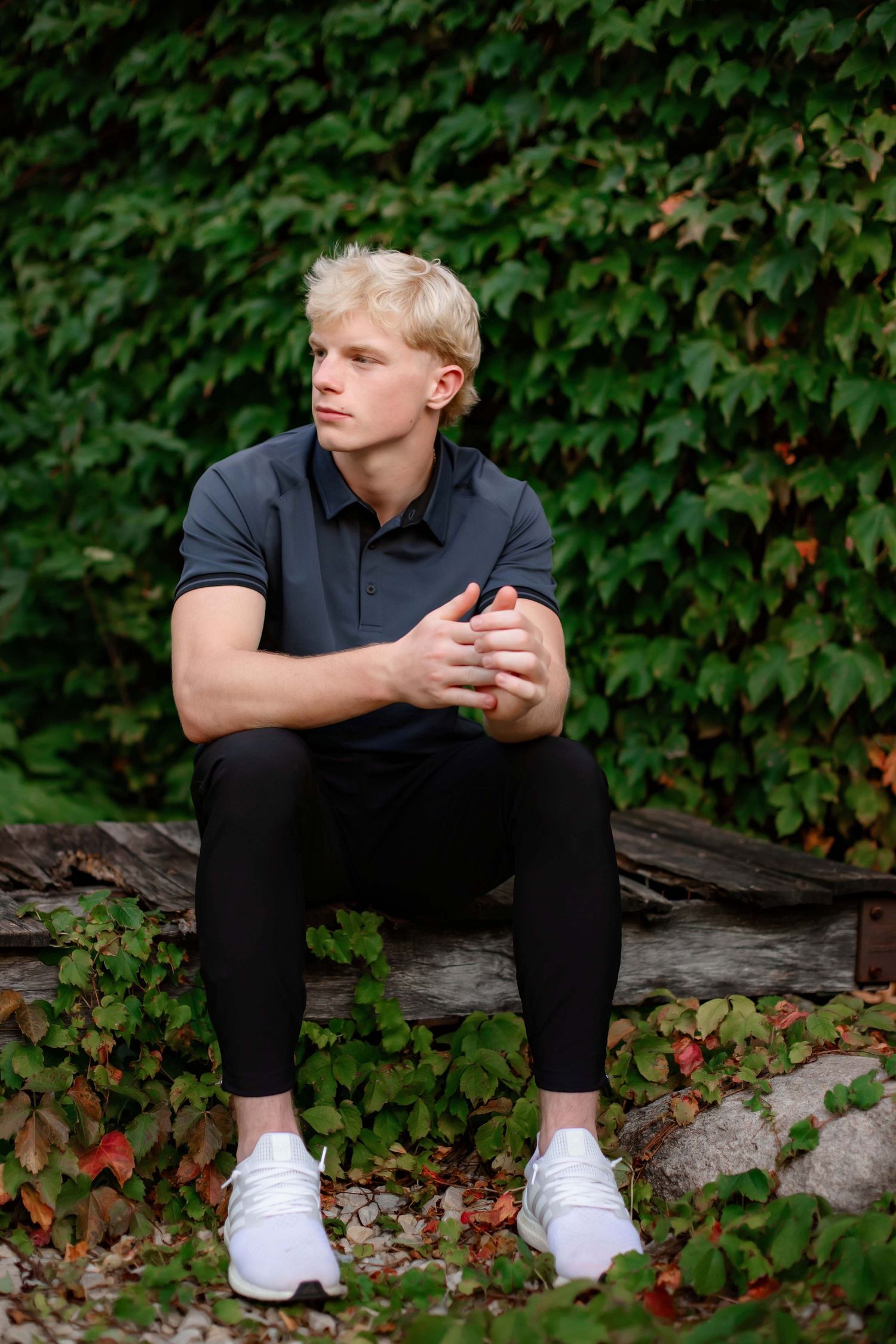 Seated outdoor portrait on rustic log with ivy background.