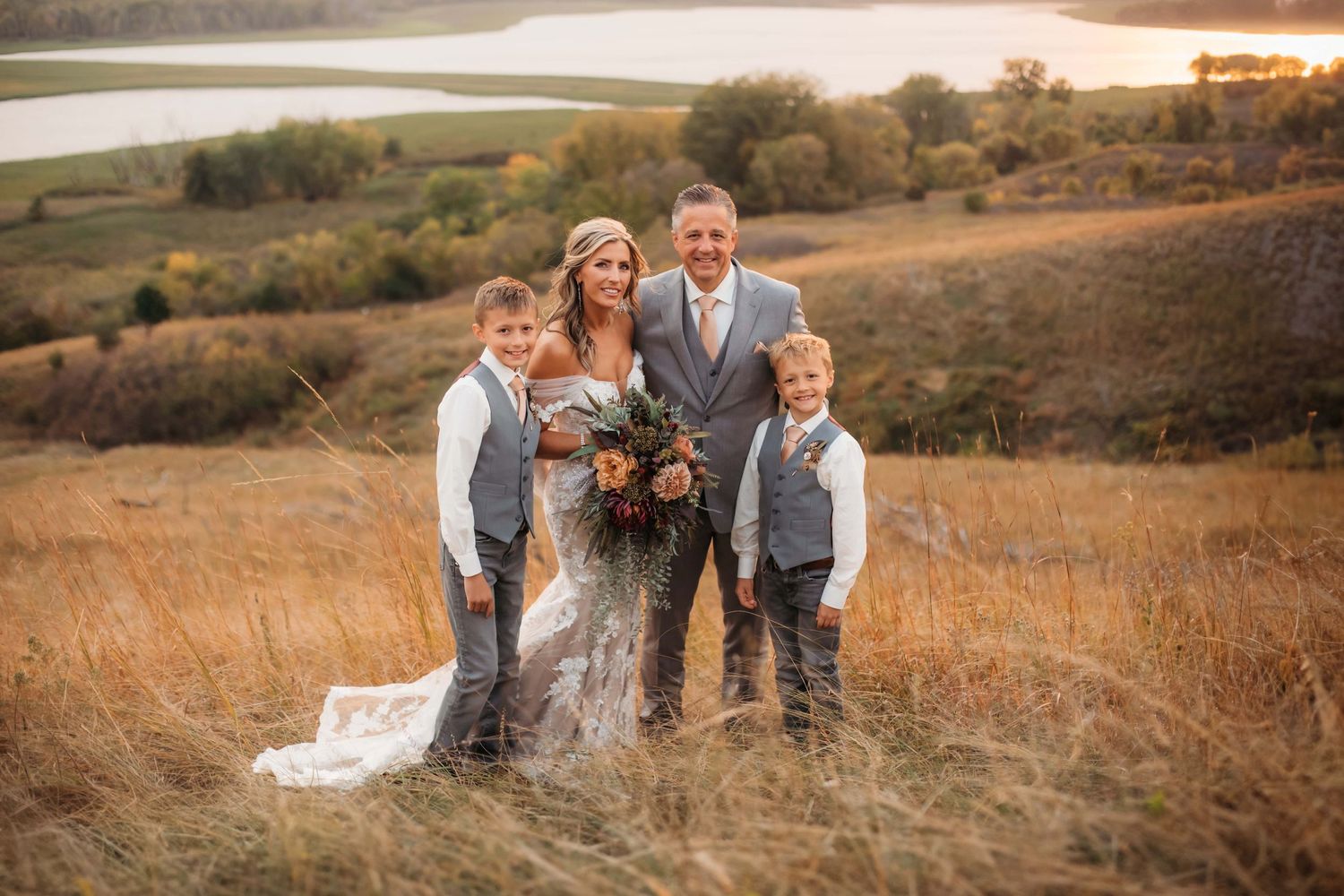 Wedding photo of family posing together in golden field with lake backdrop.