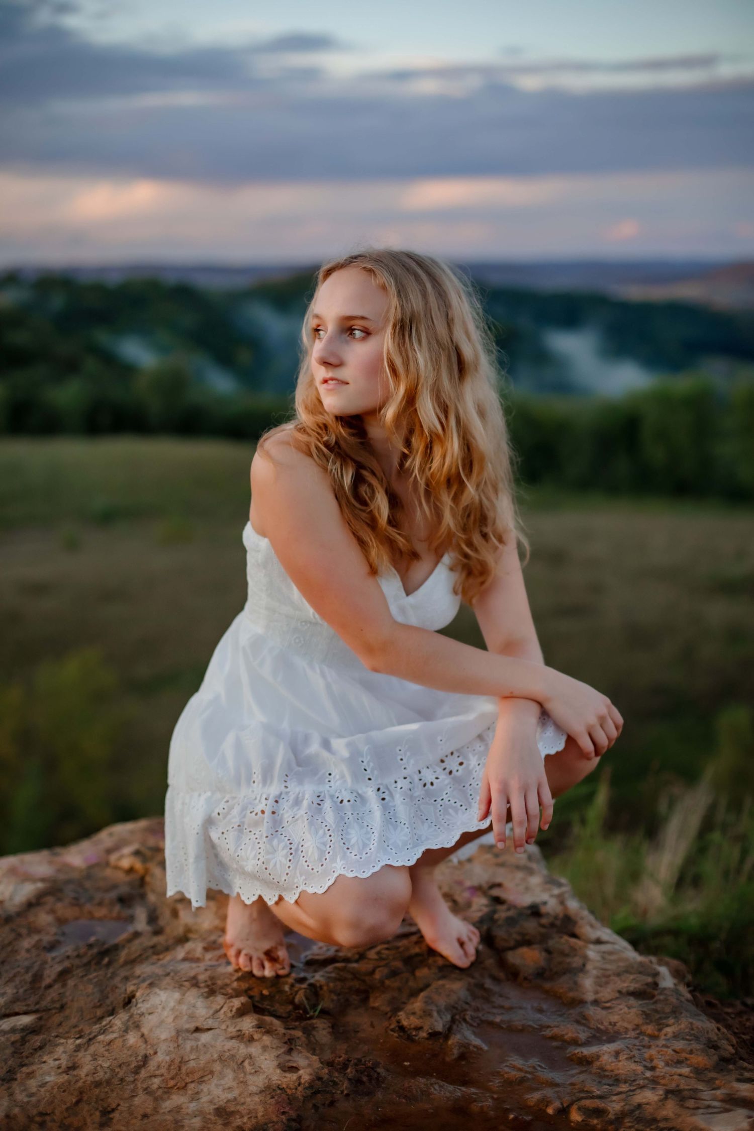 A sunset portrait on rocks overlooking misty valleys in an ethereal white dress.