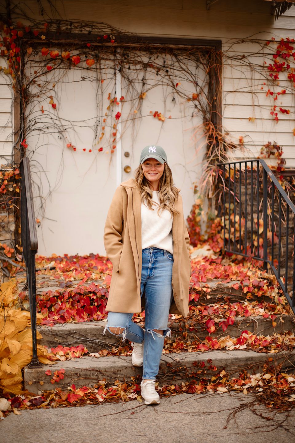 Autumn scene with red ivy vines framing a casual outfit against white wall entrance.