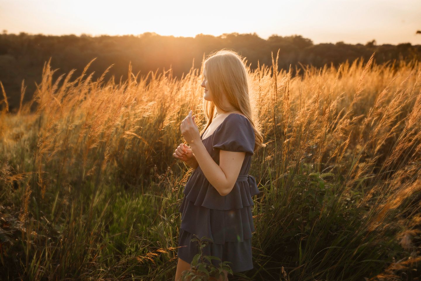 A silhouette stands in tall grass during golden hour sunset.