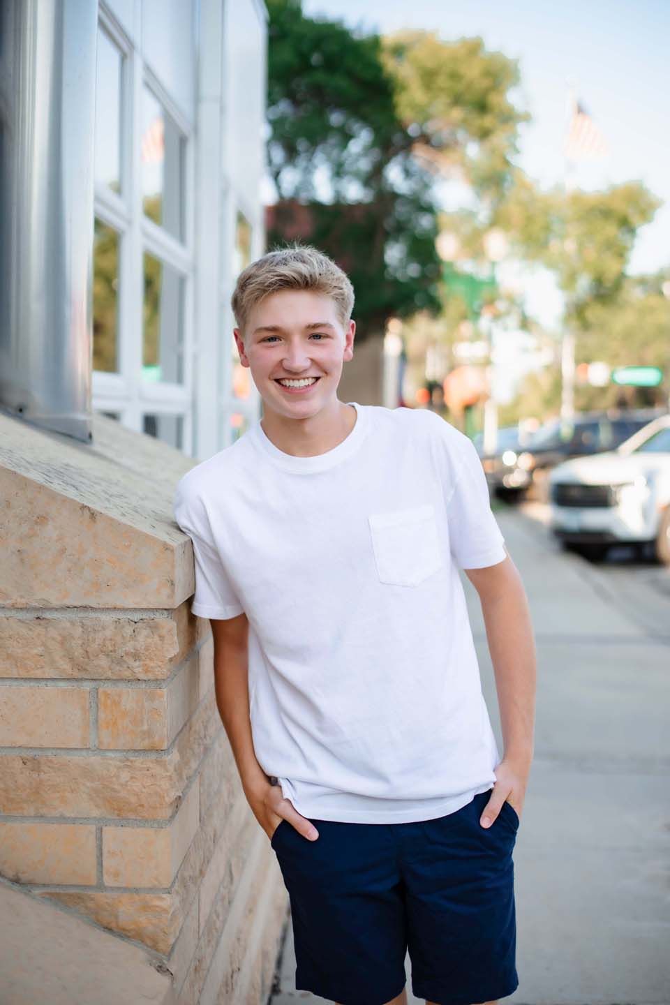 Casual portrait against stone wall with white t-shirt and navy shorts in urban setting.