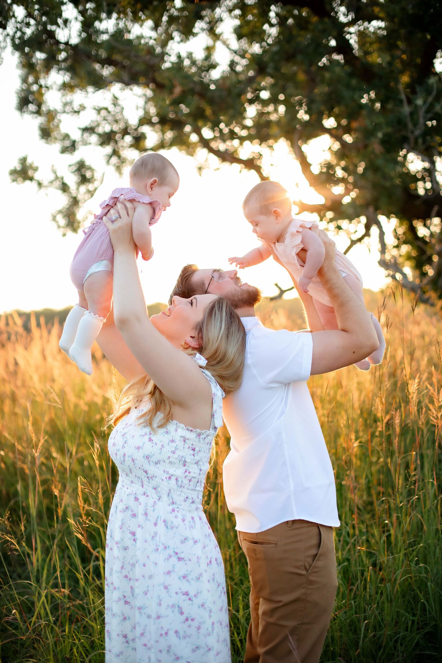 Parents playfully lifting babies in air during golden hour photoshoot in meadow.