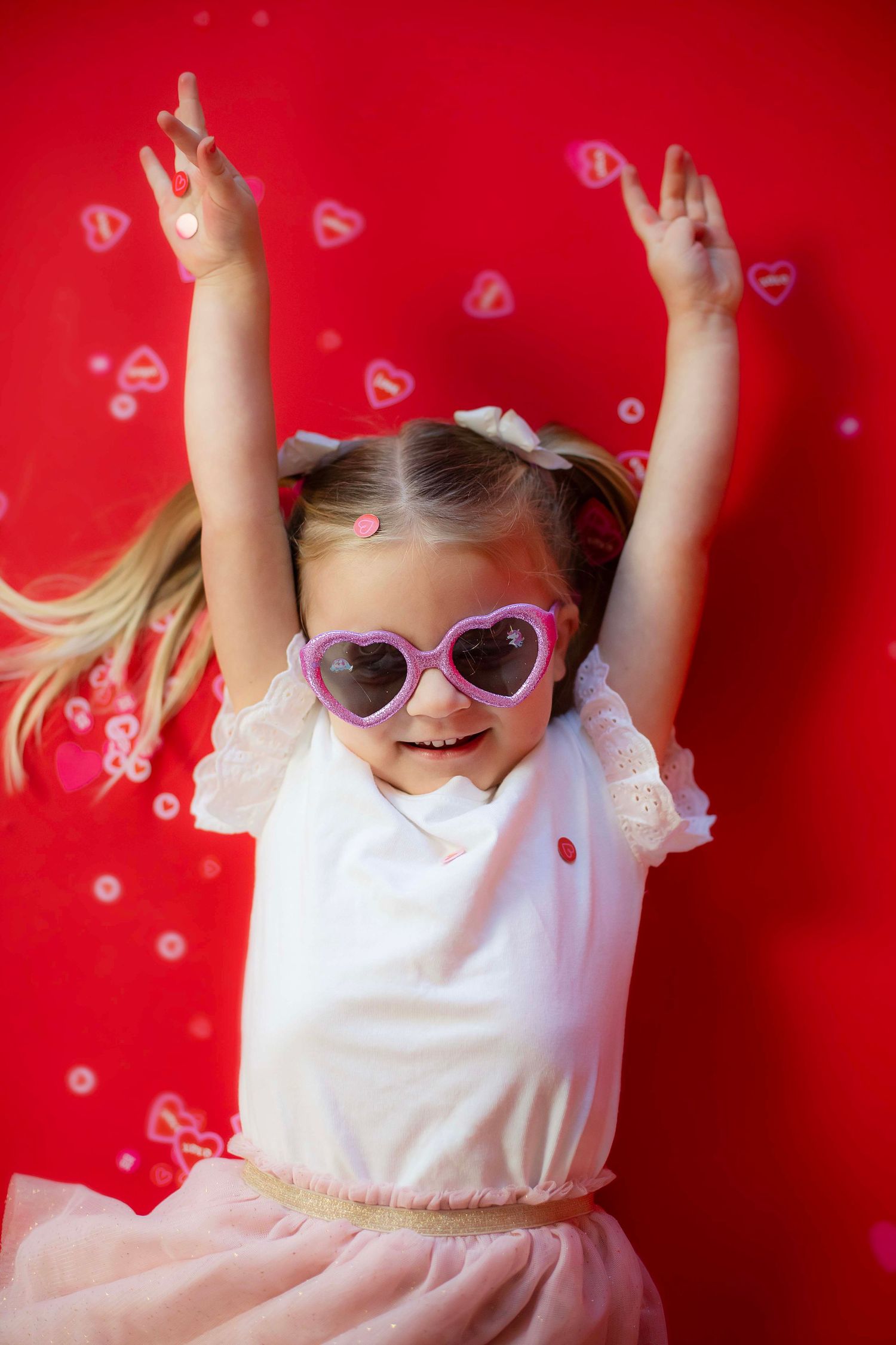 Energetic pose in tulle skirt and heart sunglasses against red background with floating hearts.
