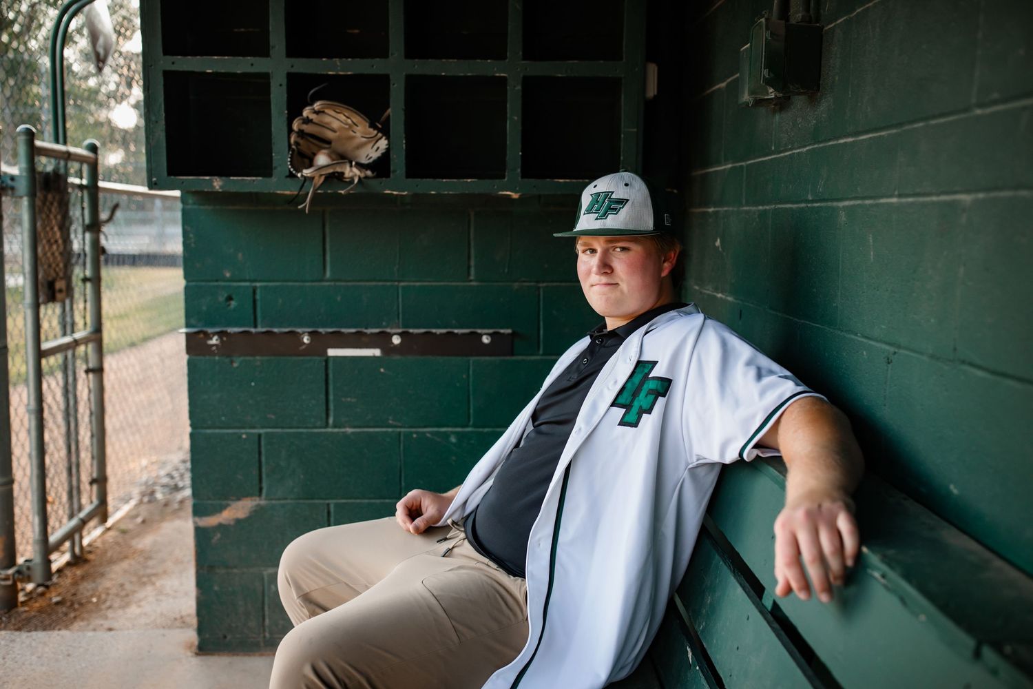 Baseball player relaxing in green dugout with equipment.