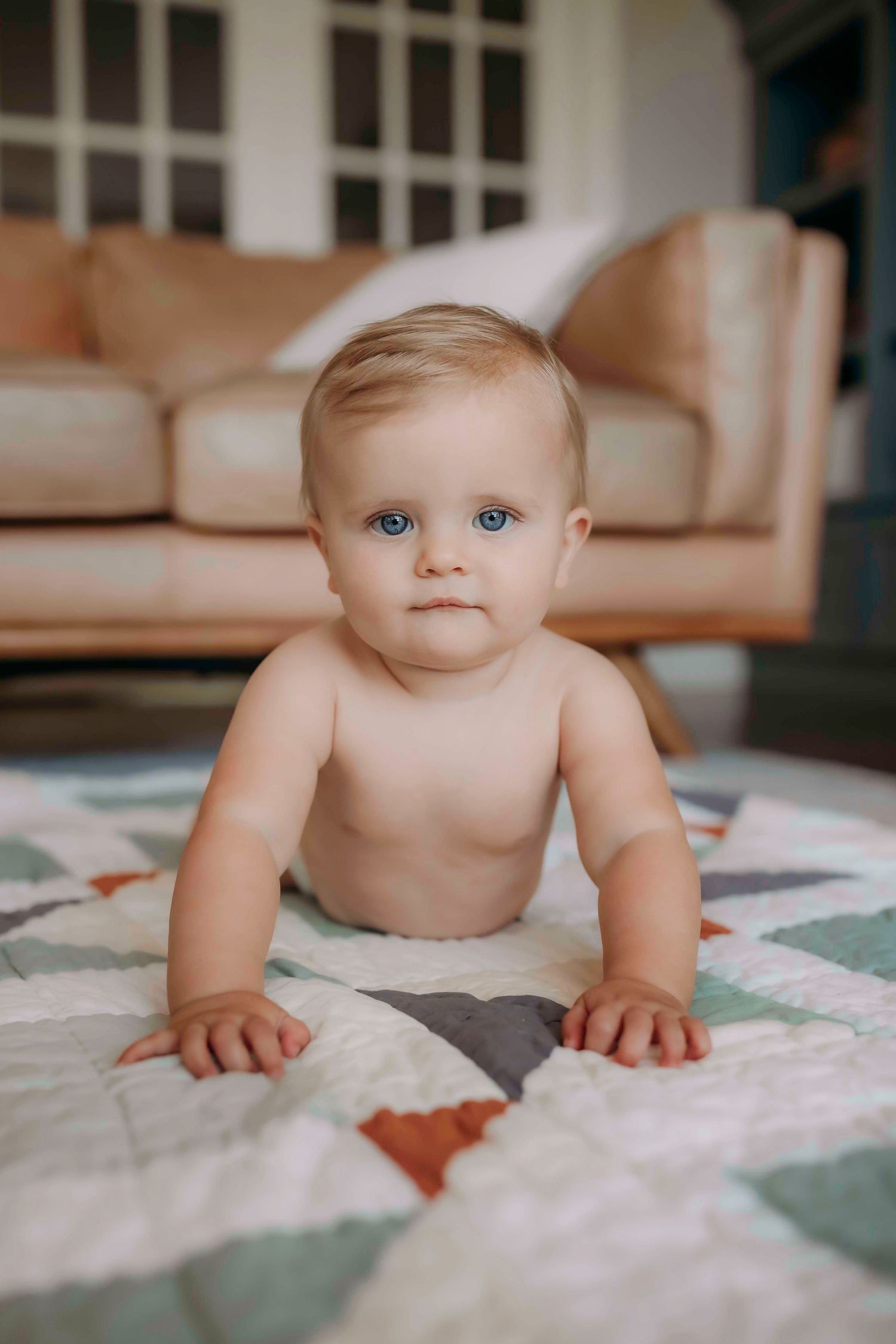 A baby crawls on a patchwork quilt in a sunny living room.