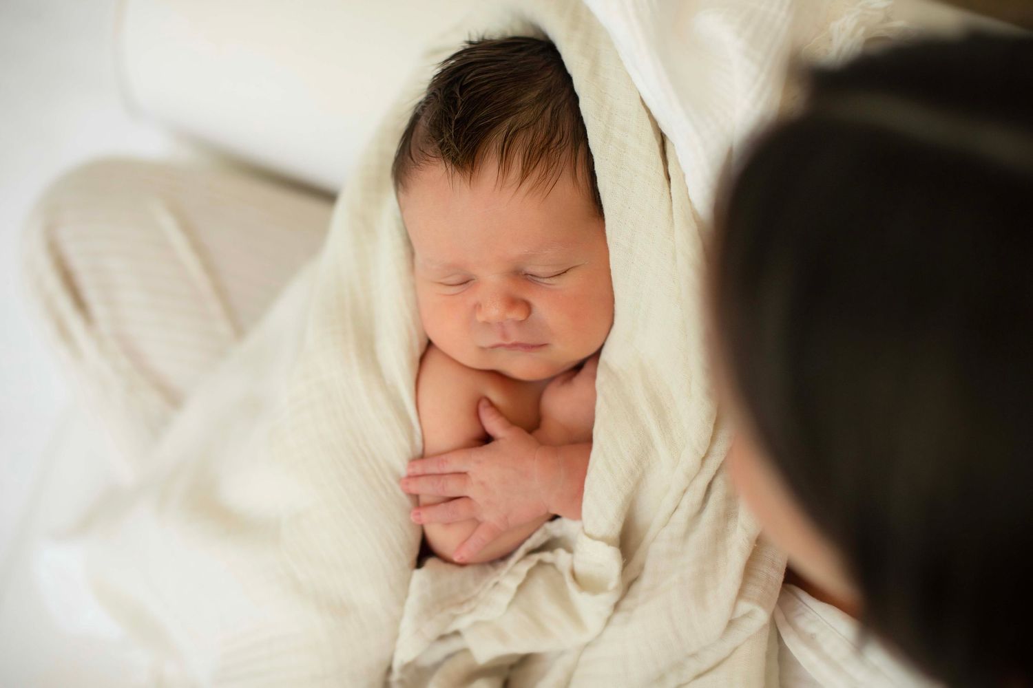 Newborn baby sleeping peacefully wrapped in a soft white blanket, cradled in a parent's arms.