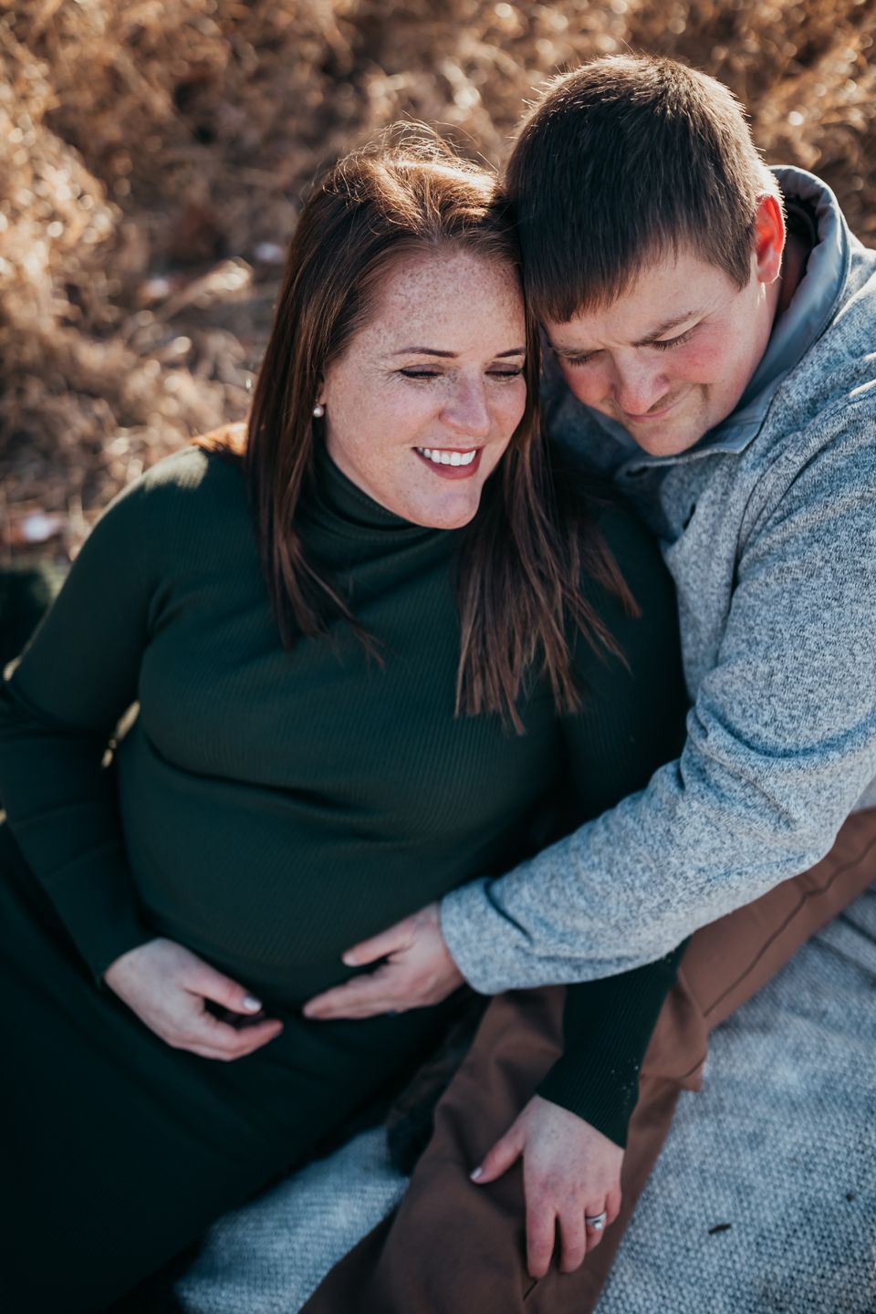 A couple sharing an intimate moment outdoors, laughing together while wearing warm sweaters against a natural background.