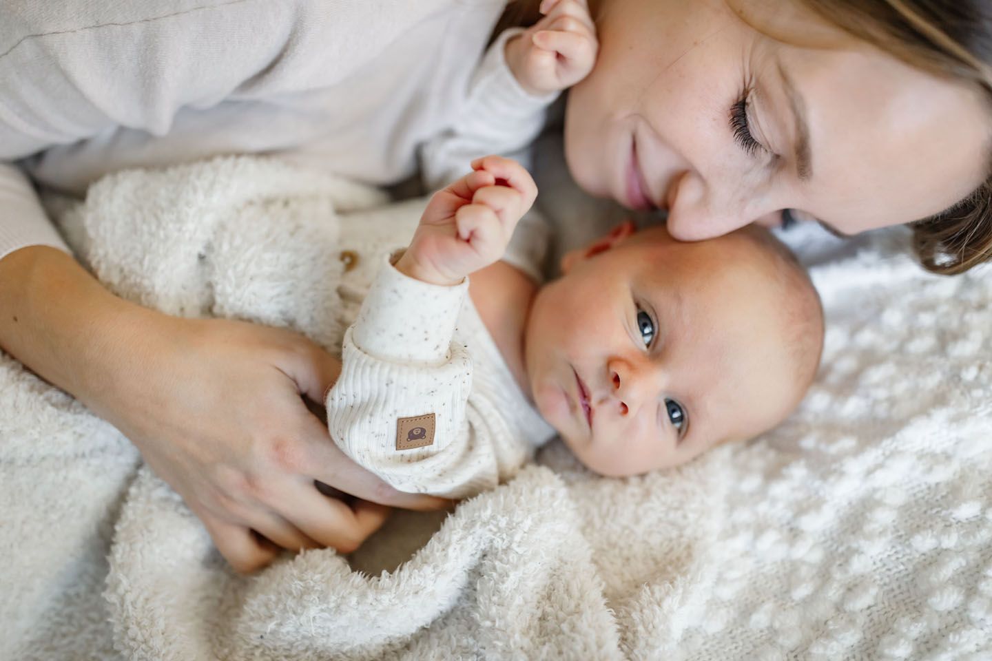 Tender moment on white bedding with infant in soft clothing.