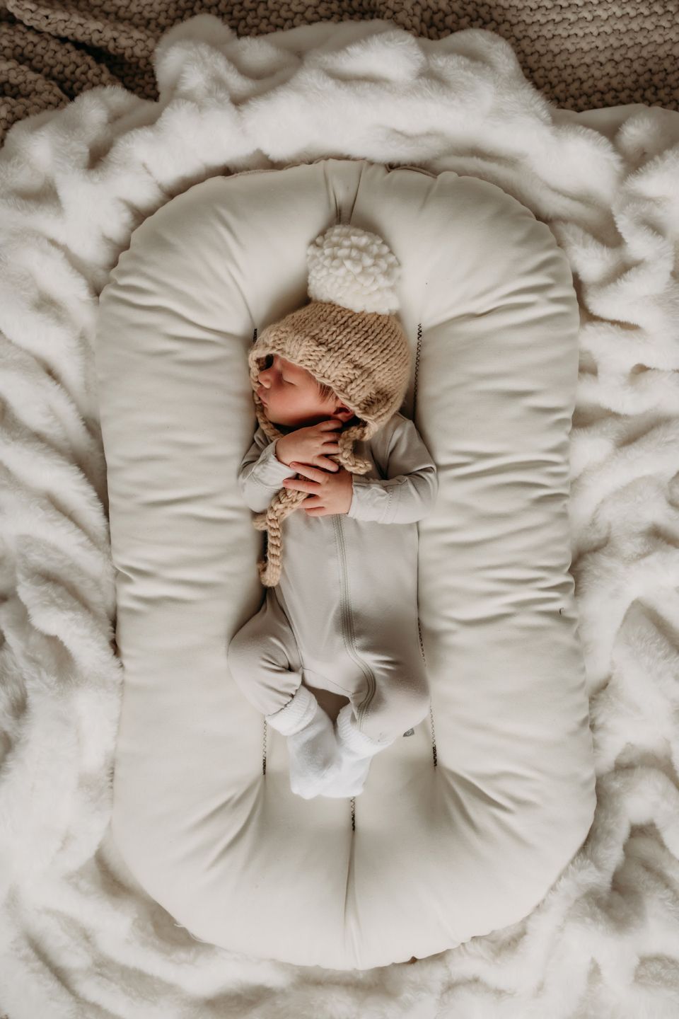 Sleeping newborn in knit hat resting in white baby lounger.