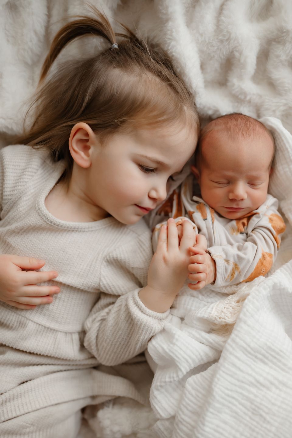 A heartwarming moment as siblings bond while lying on soft white bedding.