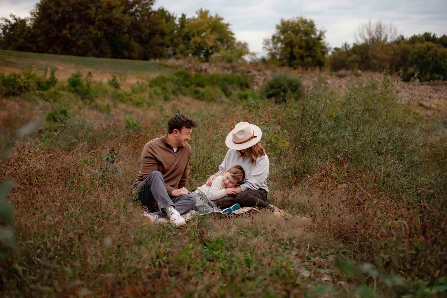 A couple sits together in a wildflower field reading a book on a sunny afternoon.