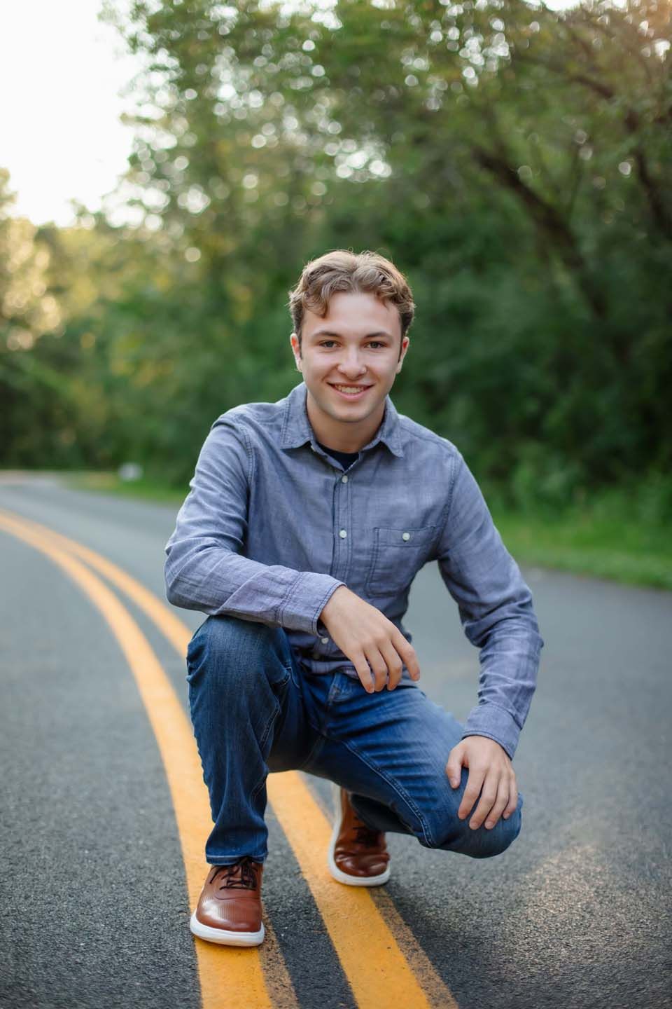 Outdoor portrait on yellow road line wearing chambray shirt and jeans.