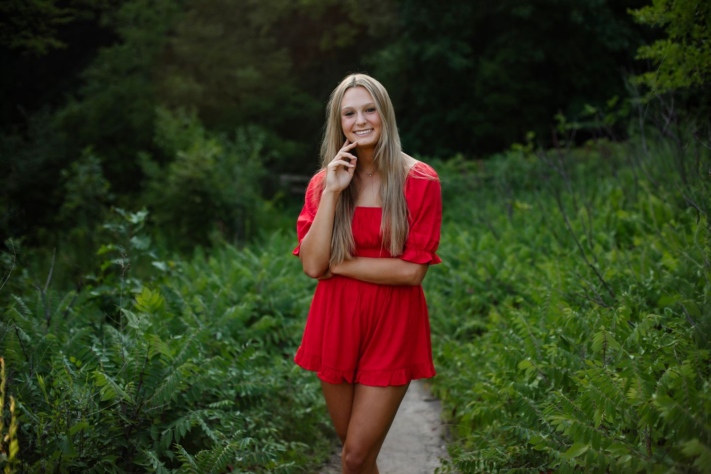 Someone posing in a bright red romper on a green nature path during summer.