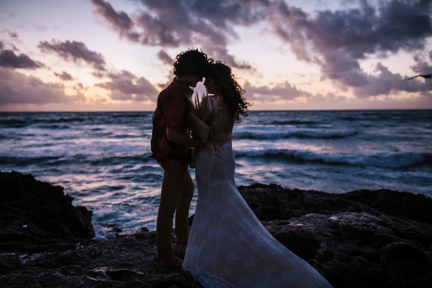 Silhouetted couple embraces against a vibrant sunset over rocky coastal waters.