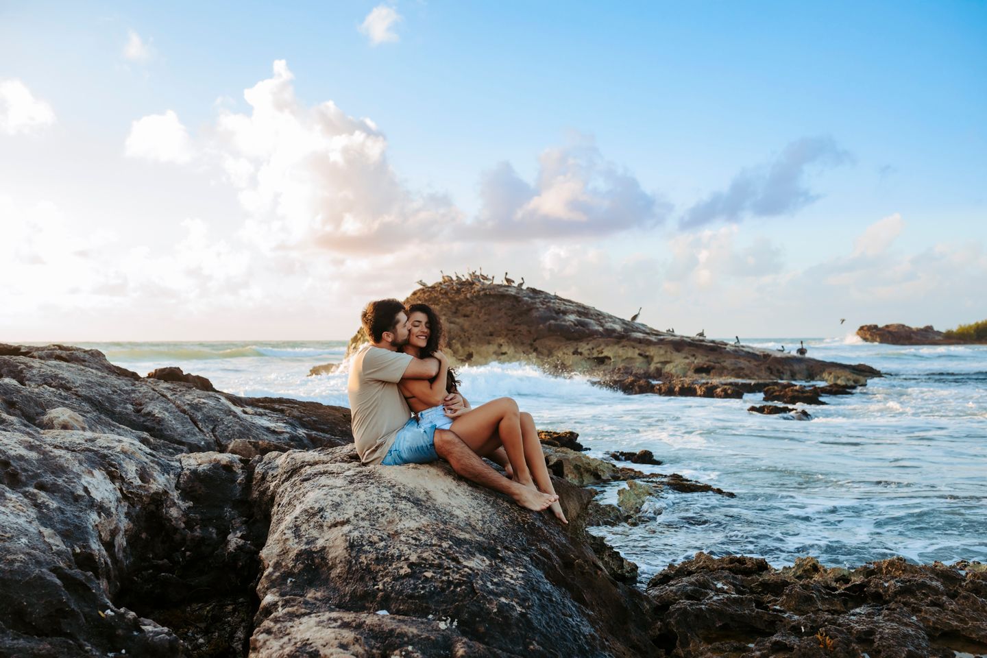 Couple relaxing on rocky outcrop overlooking ocean during Tulum sunrise.
