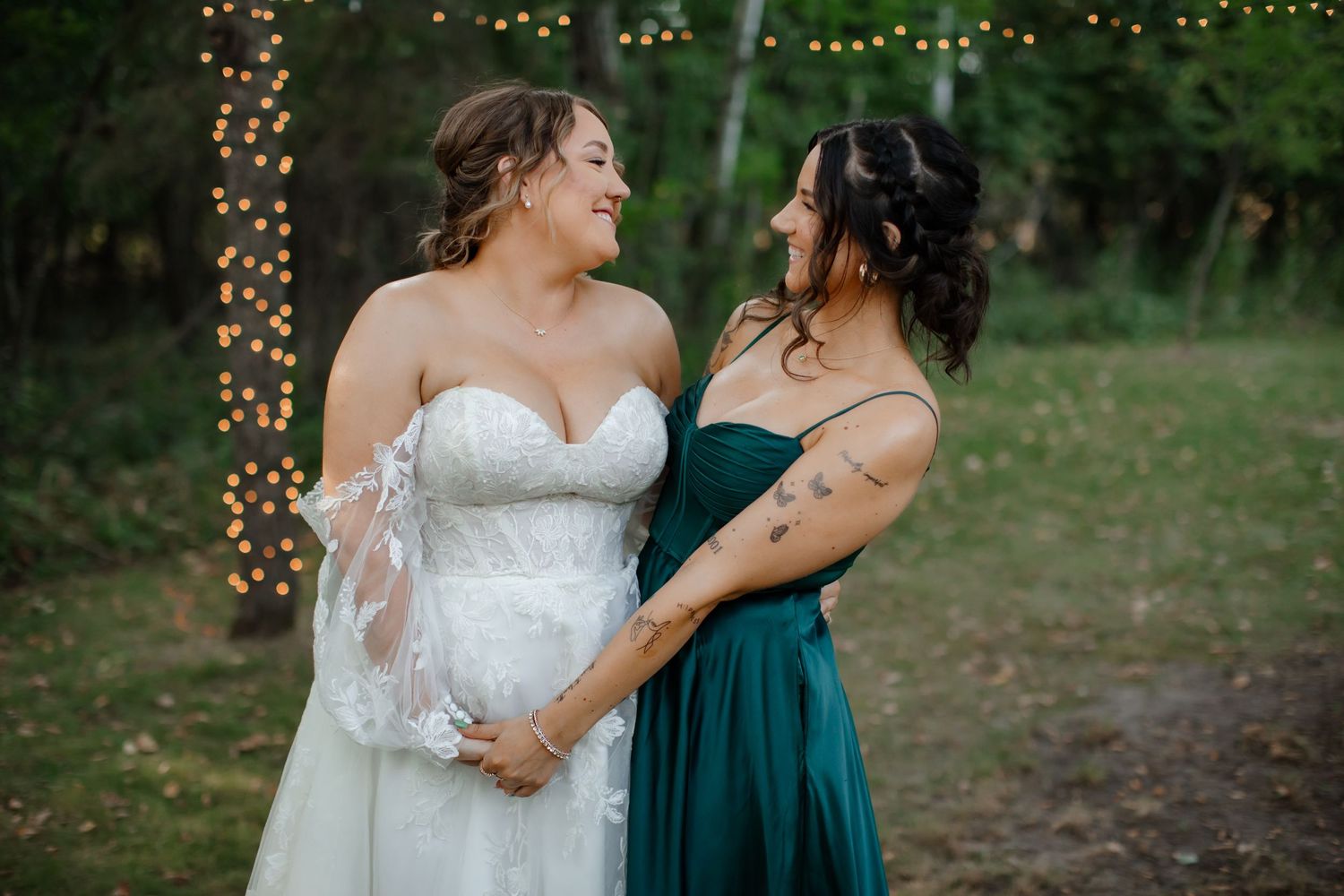 Sweet moment between a bride and bridesmaid in emerald green against a forest backdrop.