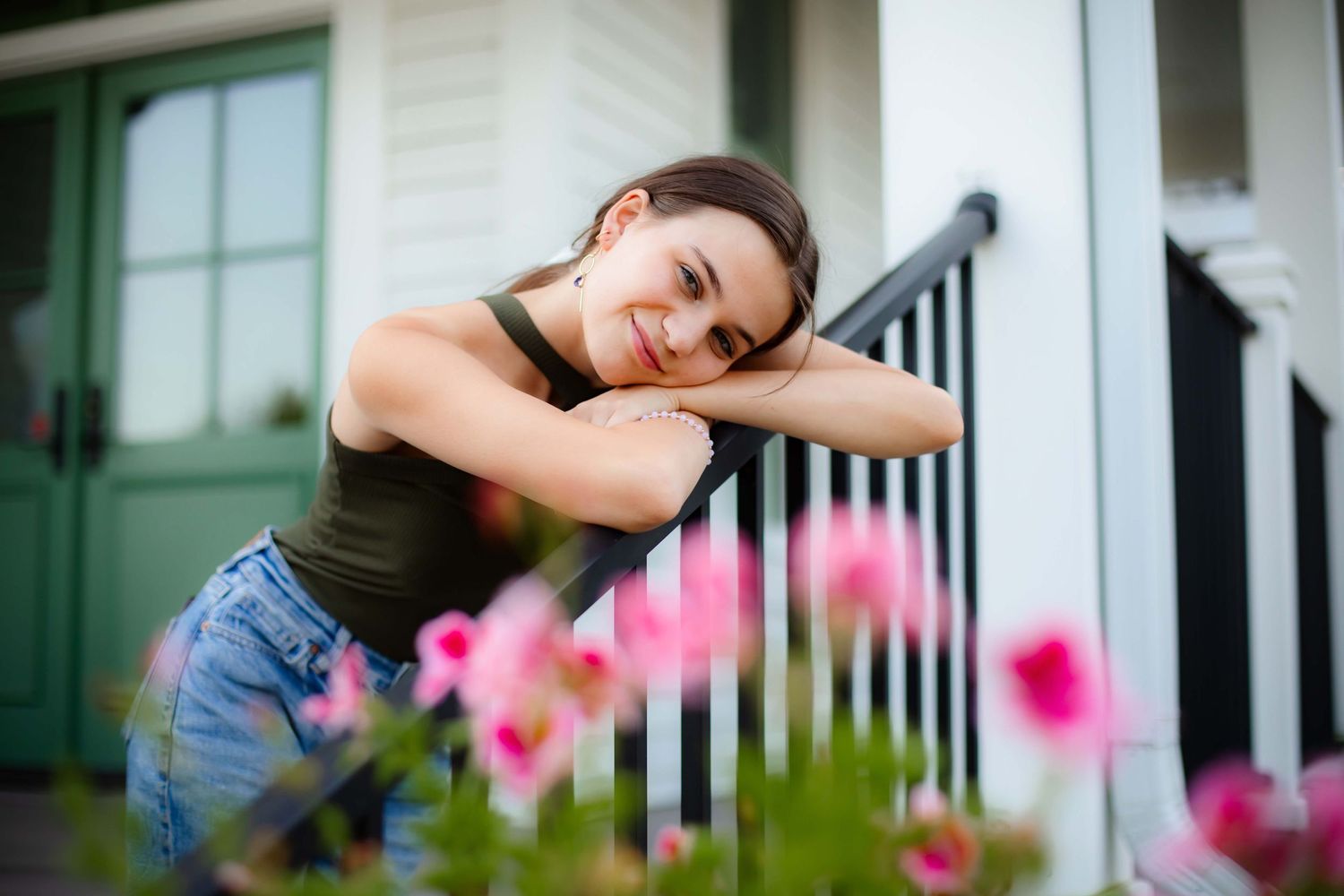 Person in casual wear leaning against railing with pink flowers in foreground.
