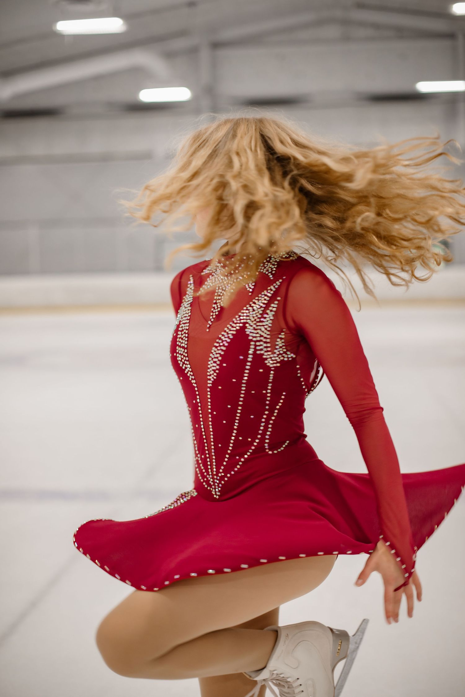 Dynamic action shot of ice skater spinning in red crystal costume with hair in motion.