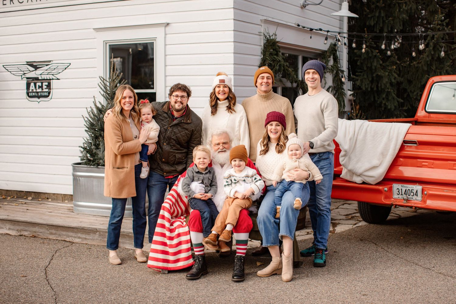 Holiday family portrait taken outdoors with a vintage red truck and white building backdrop.