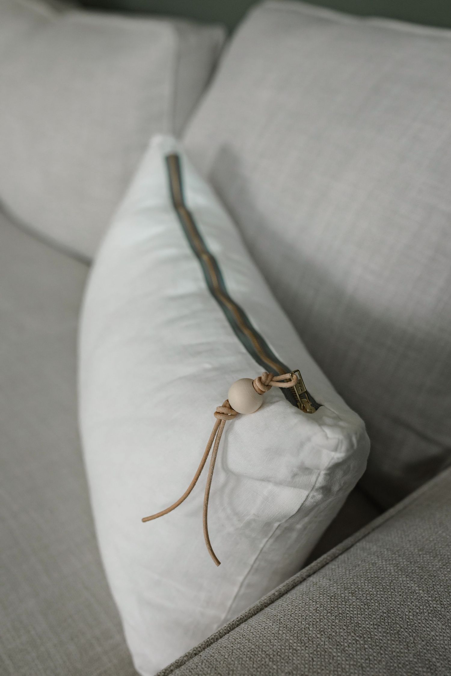 White linen pillow on grey couch with leather strap detail.