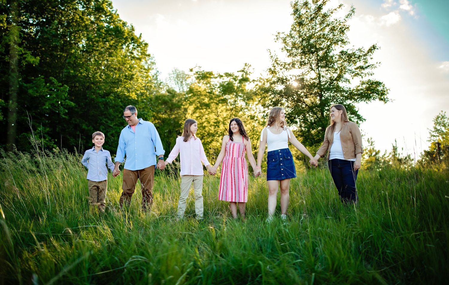 Family walking together through a sunlit meadow on a summer evening.