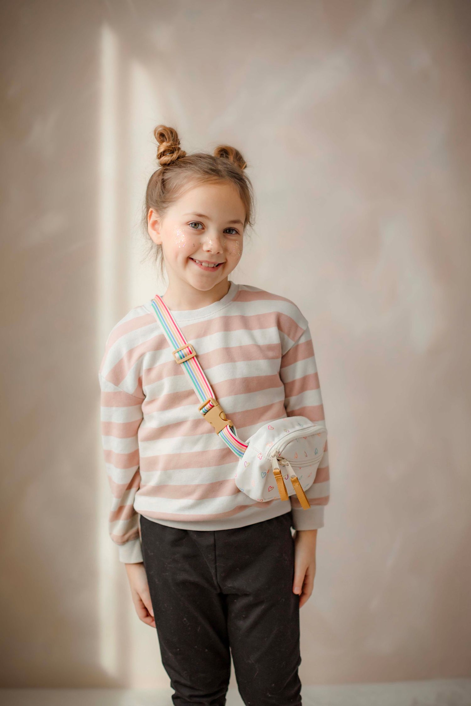 Child wearing pink striped sweater and dark pants poses playfully in studio portraits.