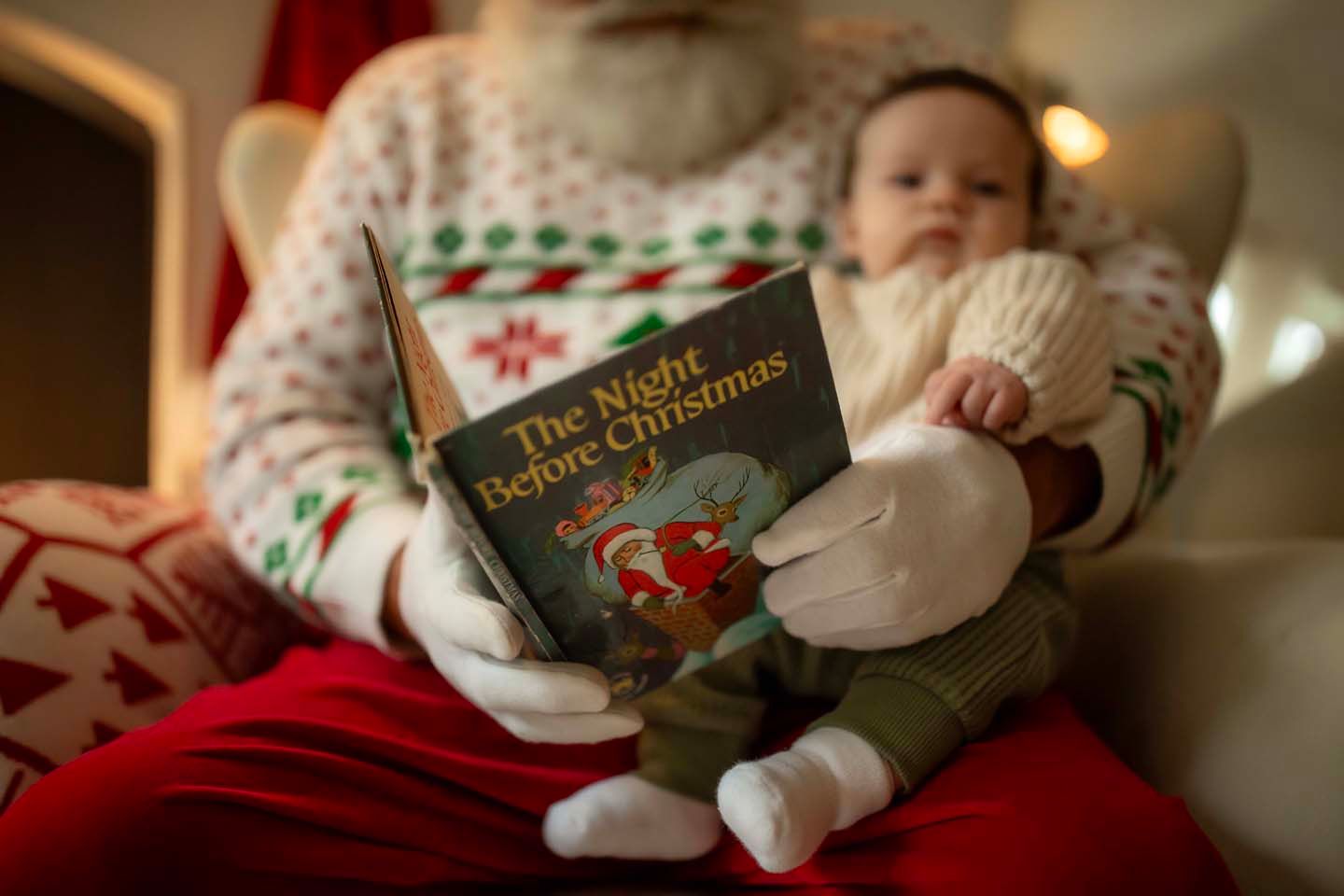 Santa Claus holding a baby while reading The Night Before Christmas book during a festive holiday photo session.