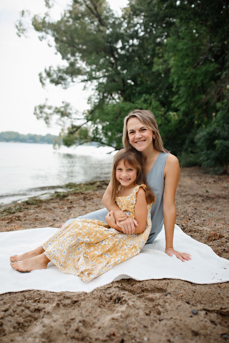 A peaceful beach scene with two people relaxing on a white blanket by the water's edge on a summer day.