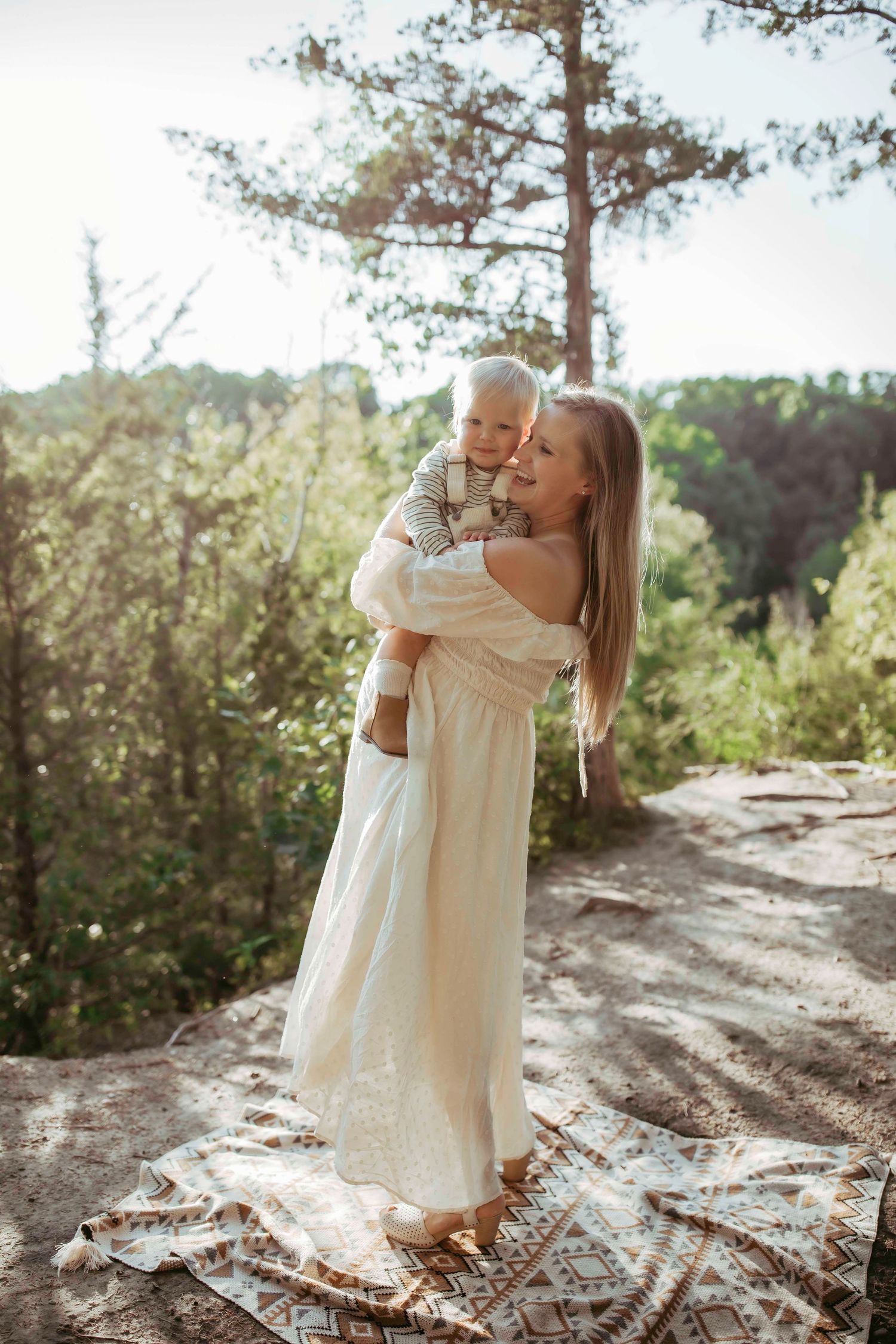 A tender outdoor portrait with a flowing white dress against a sunlit forest backdrop.