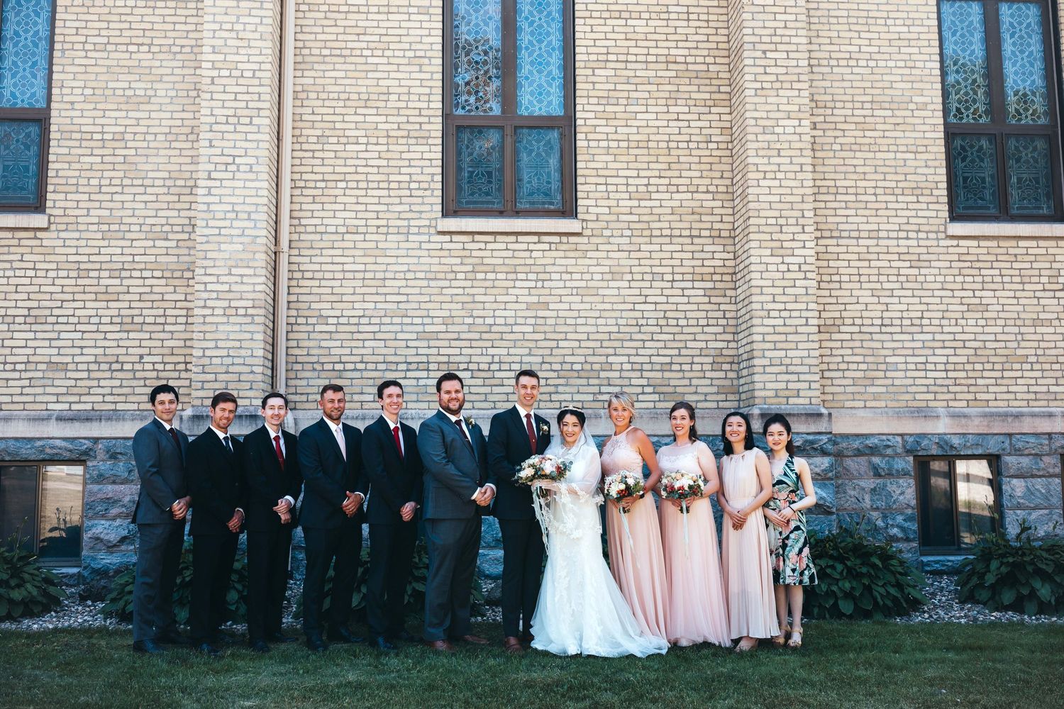 Wedding party group photo lined up against church exterior.