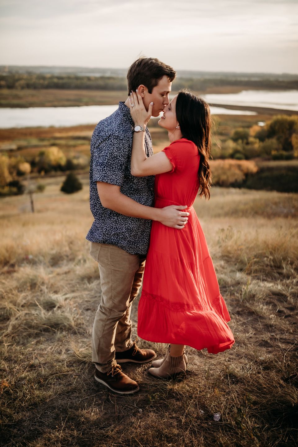 A tender embrace captured on a hillside with autumn colors and water in the background.
