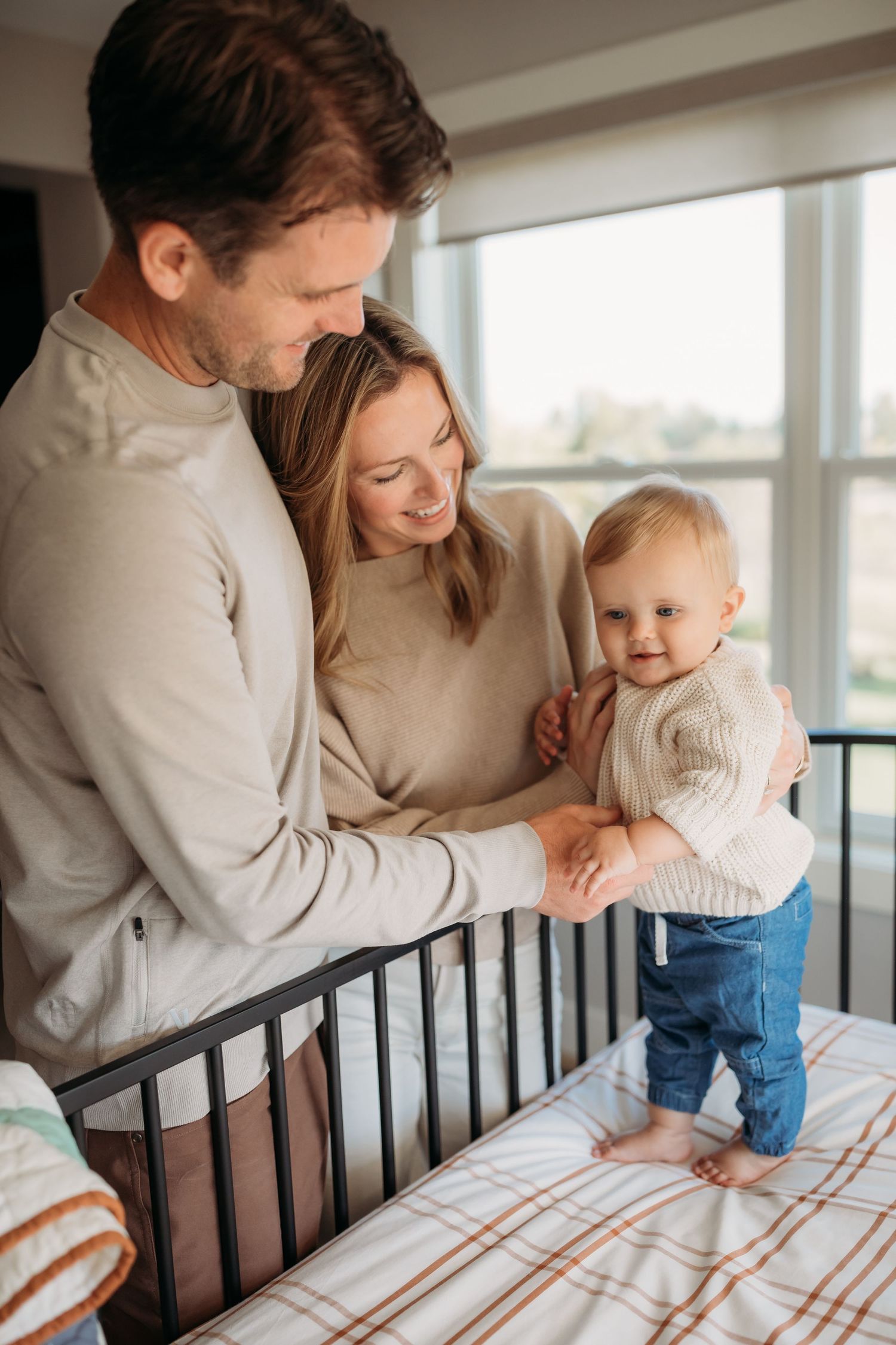 A tender family moment captured beside a crib in natural light.
