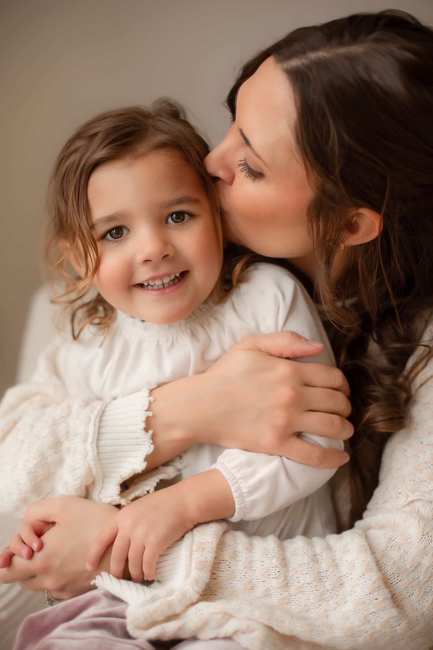 A tender moment between parent and child cuddling and laughing together on white bedding.